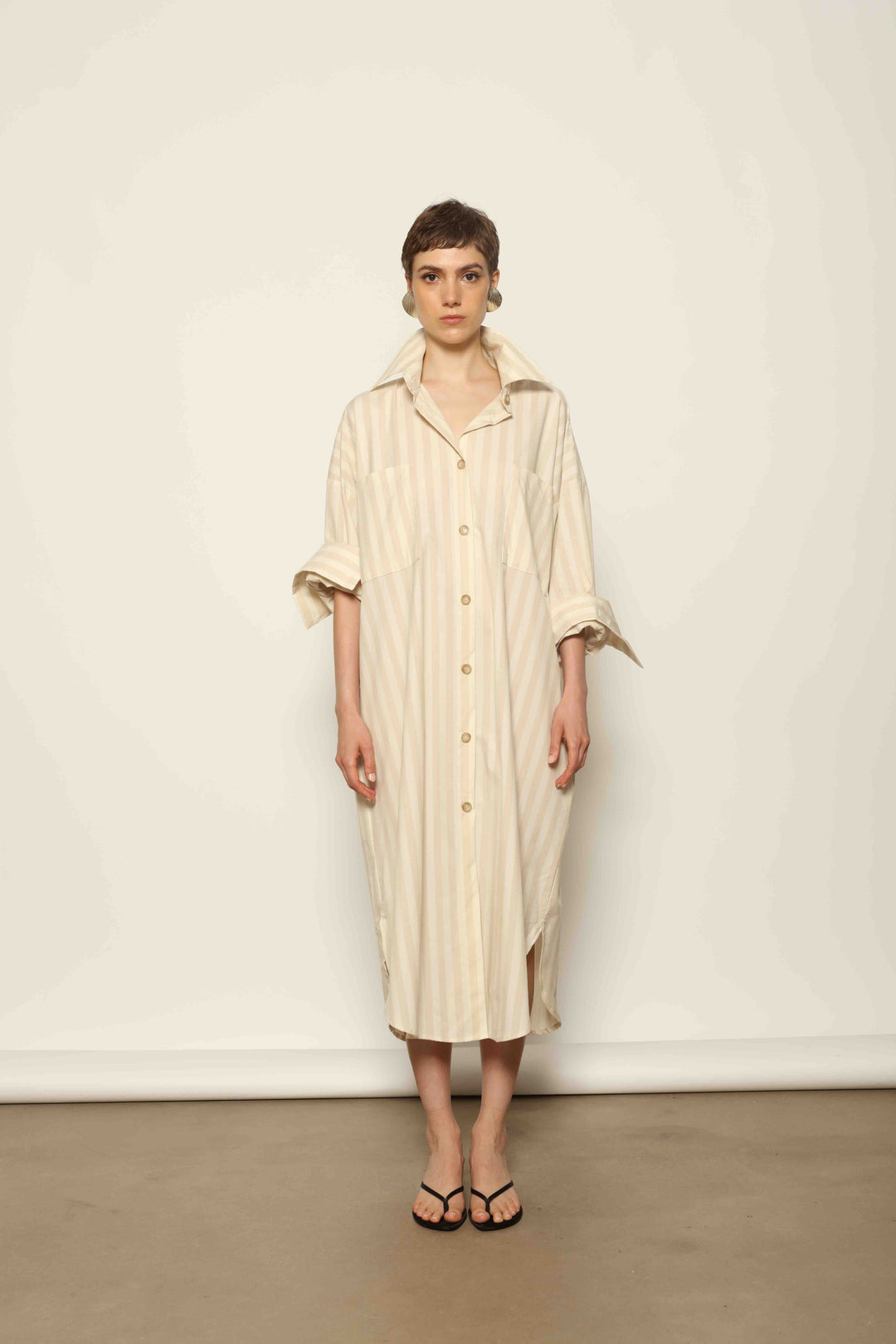 Model is wearing the Sand White Striped Bettina Dress by House of Nomad Stories, featuring a fluid silhouette with subtle sand and white vertical stripes and a soft, elegant drape.