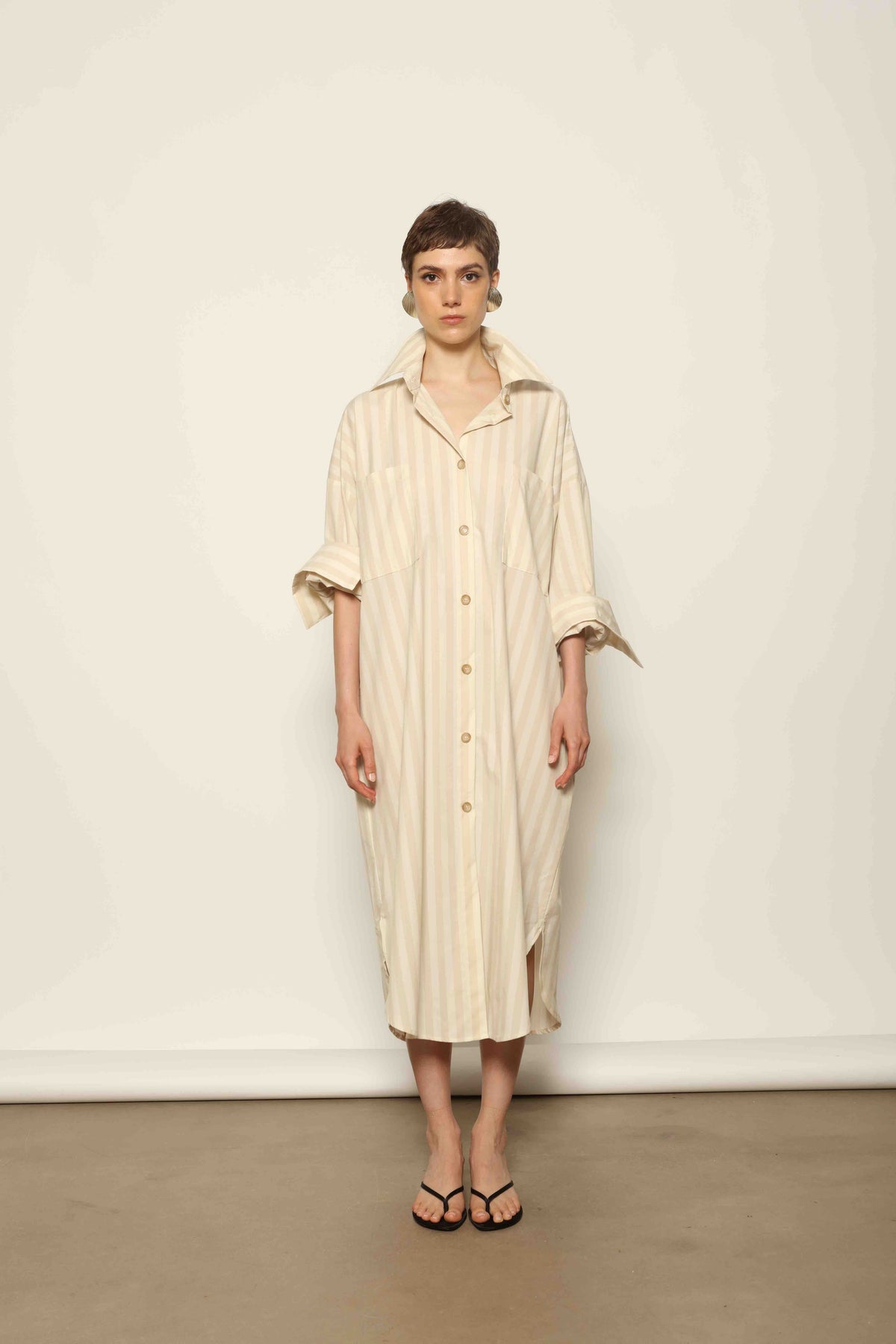 Model is wearing the Sand White Striped Bettina Dress by House of Nomad Stories, featuring a fluid silhouette with subtle sand and white vertical stripes and a soft, elegant drape.