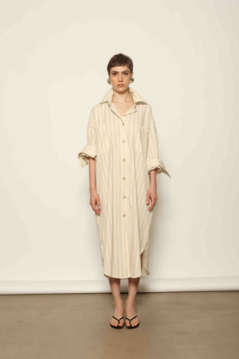 Model is wearing the Sand White Striped Bettina Dress by House of Nomad Stories, featuring a fluid silhouette with subtle sand and white vertical stripes and a soft, elegant drape.