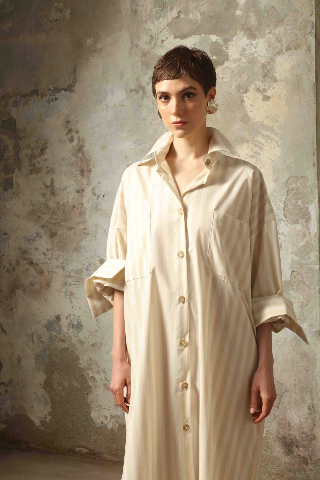 Model is wearing the Sand White Striped Bettina Dress by House of Nomad Stories, featuring a fluid silhouette with subtle sand and white vertical stripes and a soft, elegant drape.