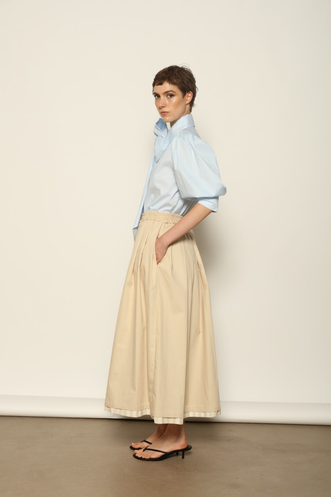 Model wearing the Seoul Camel Skirt by House of Nomad Stories, featuring a structured camel-toned fabric, high-waisted fit, and a clean tailored silhouette with defined architectural lines.