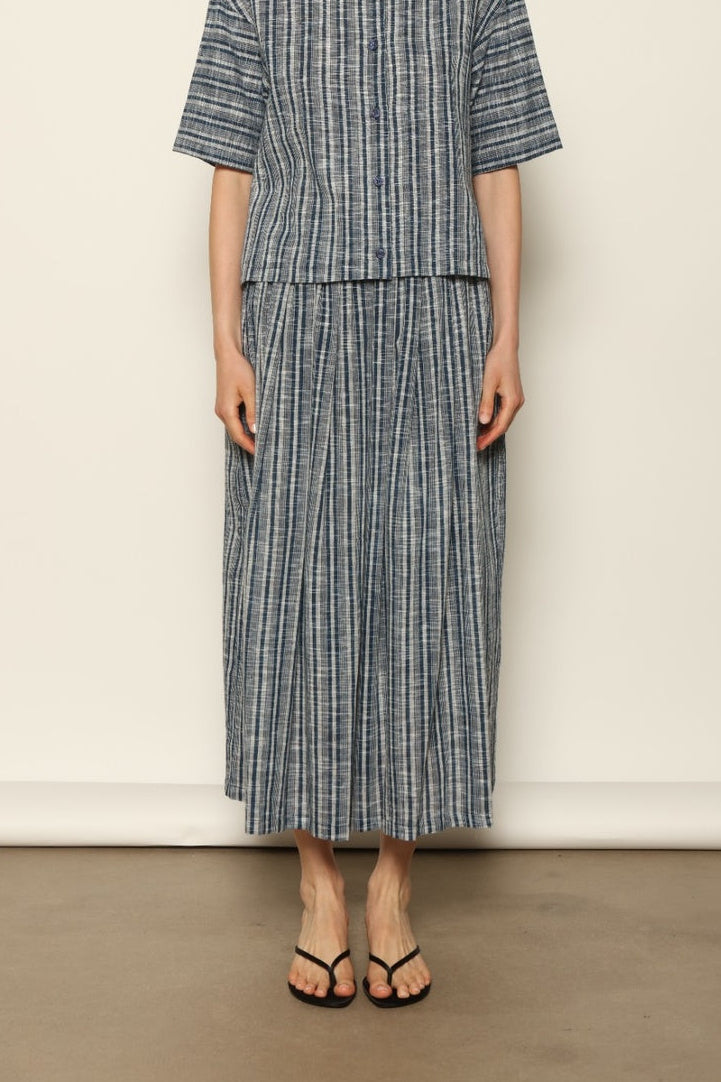 Model wearing the Seoul Indigo Blue Striped Ikat Midi Skirt by House of Nomad Stories, crafted from handwoven Kala cotton with an indigo blue and off-white ikat pattern, elasticated waistband, and relaxed midi silhouette.
