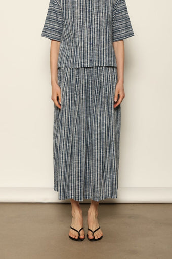 Model wearing the Seoul Indigo Blue Striped Ikat Midi Skirt by House of Nomad Stories, crafted from handwoven Kala cotton with an indigo blue and off-white ikat pattern, elasticated waistband, and relaxed midi silhouette.