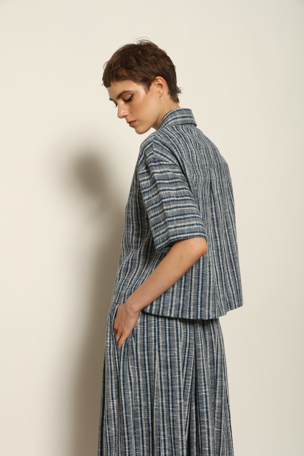 Model wearing the Seoul Indigo Blue Striped Ikat Midi Skirt by House of Nomad Stories, crafted from handwoven Kala cotton with an indigo blue and off-white ikat pattern, elasticated waistband, and relaxed midi silhouette.