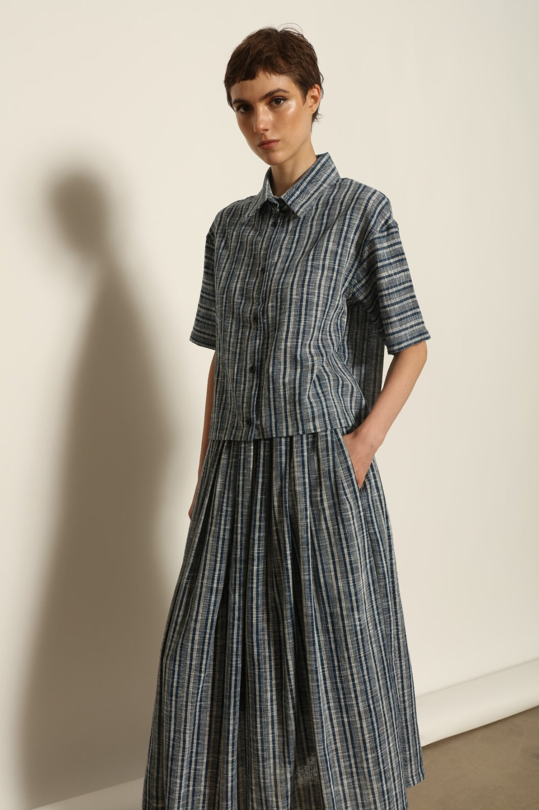 Model wearing the Seoul Indigo Blue Striped Ikat Midi Skirt by House of Nomad Stories, crafted from handwoven Kala cotton with an indigo blue and off-white ikat pattern, elasticated waistband, and relaxed midi silhouette.