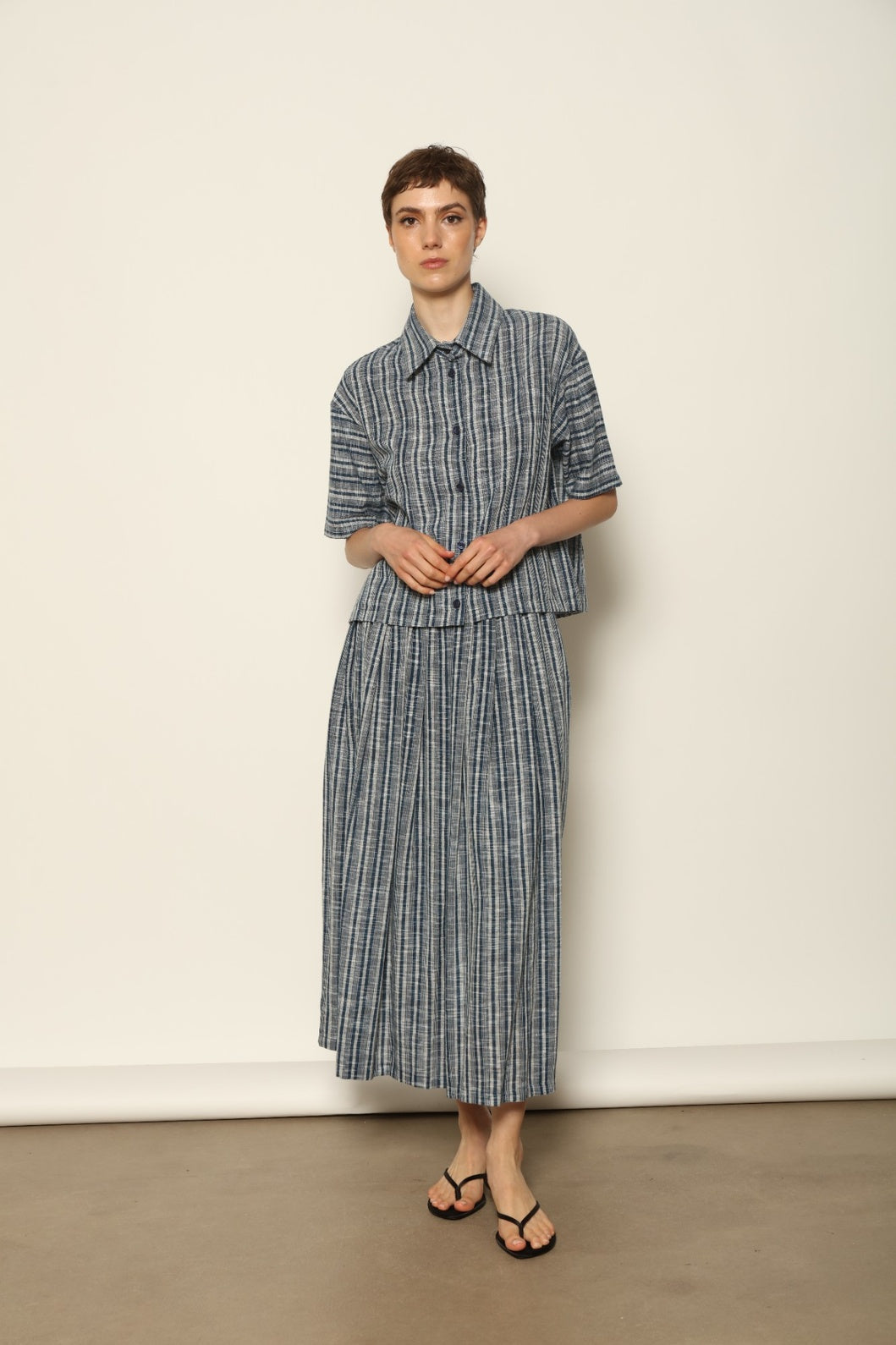 Model wearing the Seoul Indigo Blue Striped Ikat Midi Skirt by House of Nomad Stories, crafted from handwoven Kala cotton with an indigo blue and off-white ikat pattern, elasticated waistband, and relaxed midi silhouette.