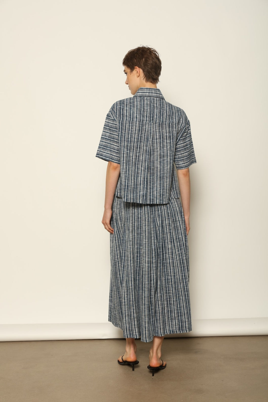 Model wearing the Emily Blue Striped Ikat Shirt by House of Woven Stories, crafted from 100% hand-loomed Kala cotton with indigo stripes, artisanal ikat pattern, and a relaxed cropped silhouette.