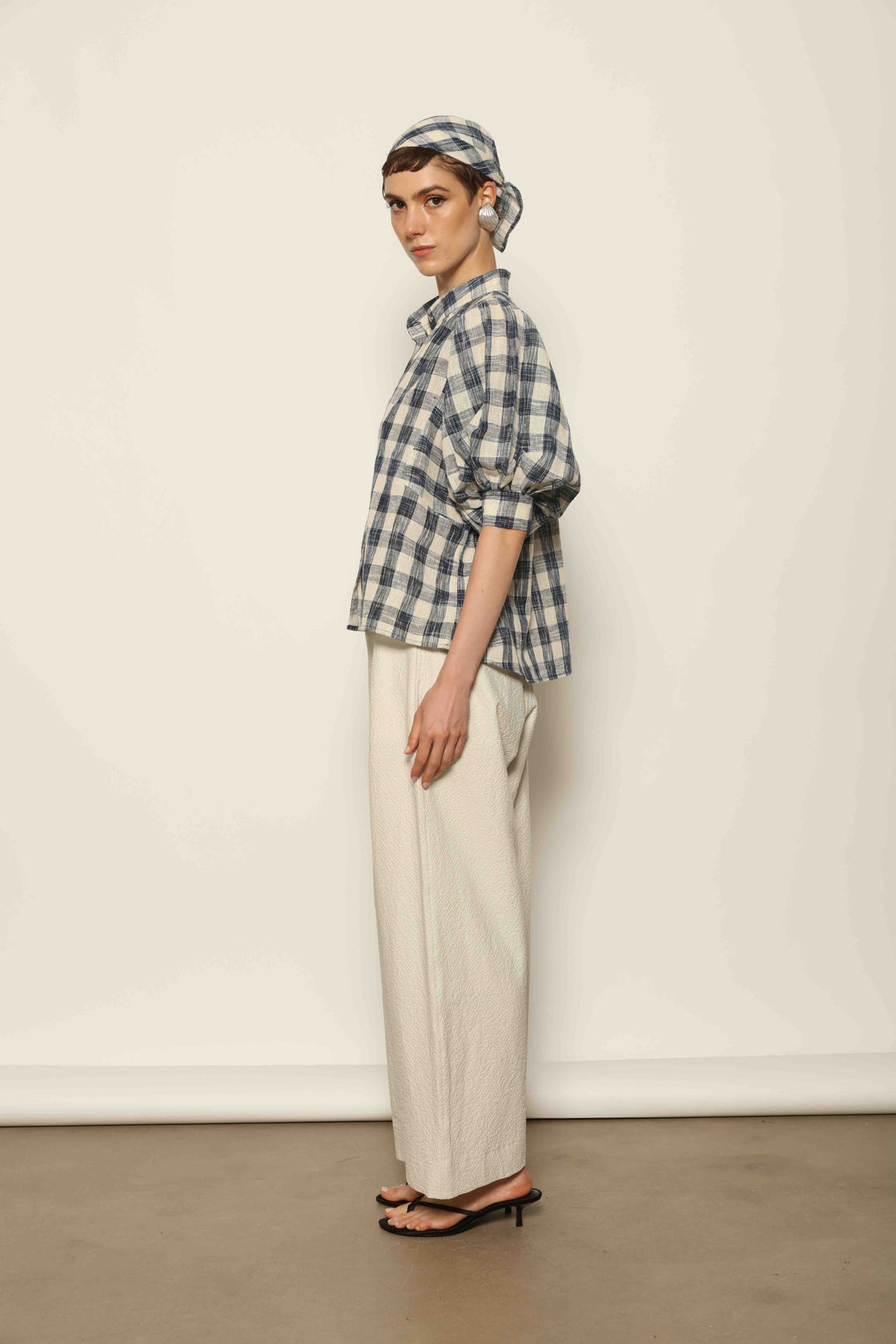 Model wearing the Lola Check Blouse by House of Woven Stories, crafted from 100% handloomed Kala cotton with a blue and white check pattern, Mandarin collar, button-front closure, and balloon sleeves.