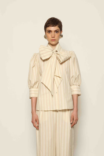 Model wearing the Karin Sand White Macro-Striped Blouse by House of Nomad Stories, featuring a relaxed fit, sand and white macro stripes, classic collar, and soft blend of cotton, merino wool, and cashmere.