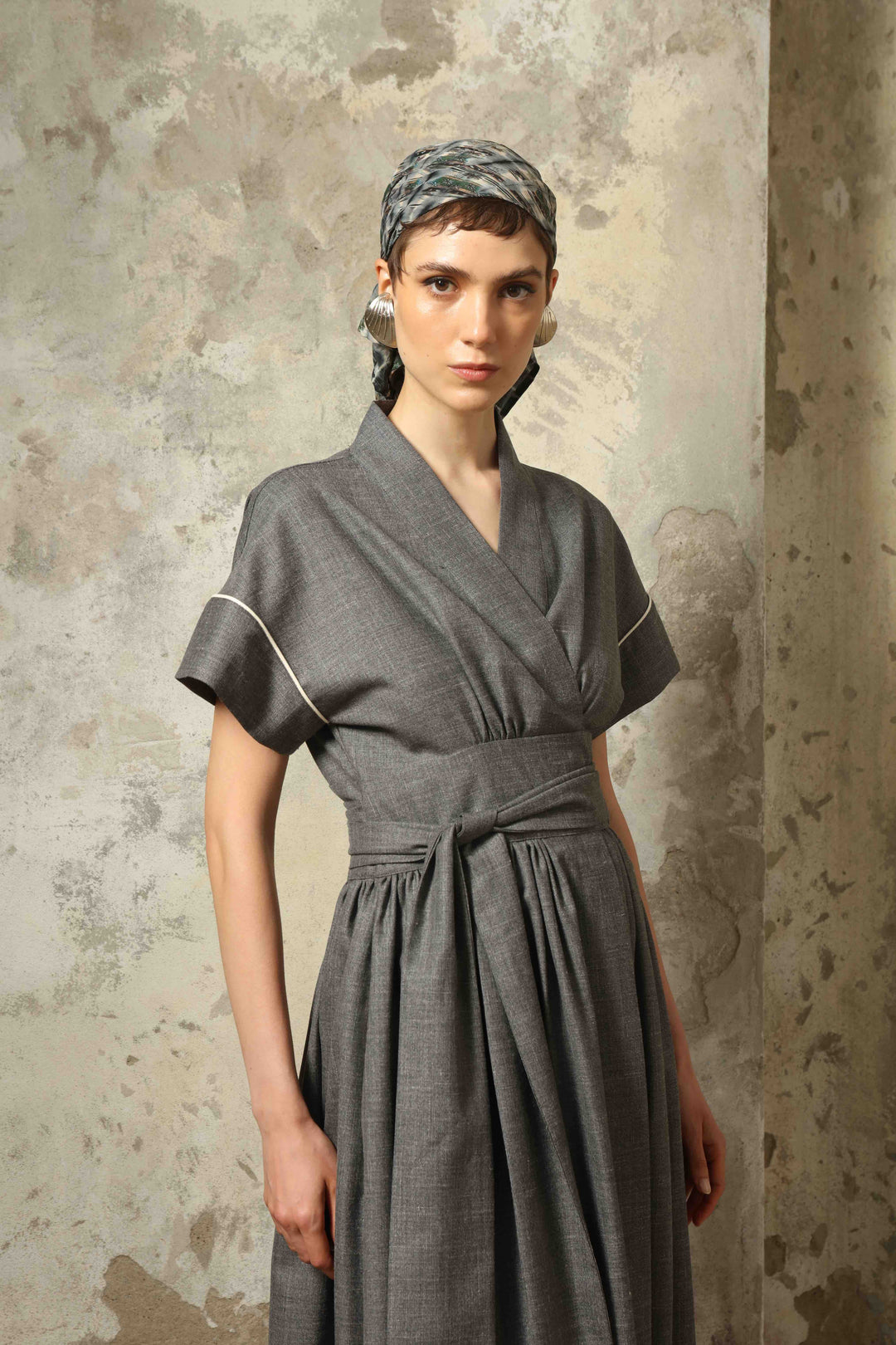 Model wearing the Saint Remy Grey Off White Midi Dress by House of Nomad Stories, featuring a wrap silhouette, adjustable belt, half sleeves, and subtle white piping detail in a fluid elegant fabric.
