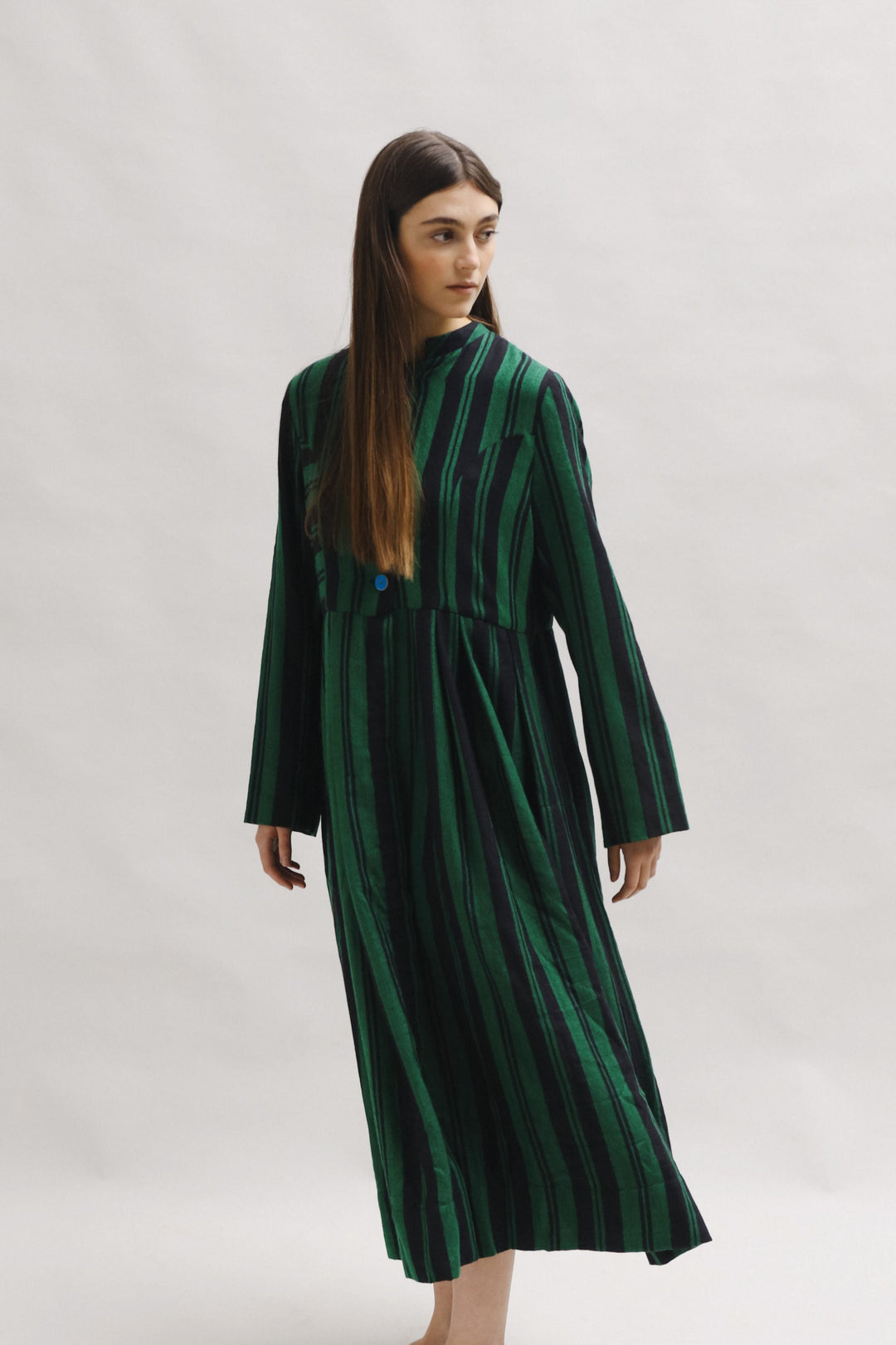Model is wearing the Folklore 34 silk and wool striped dress by Injiri, featuring bold green and black stripes and sky blue buttons, artisan-made in India.