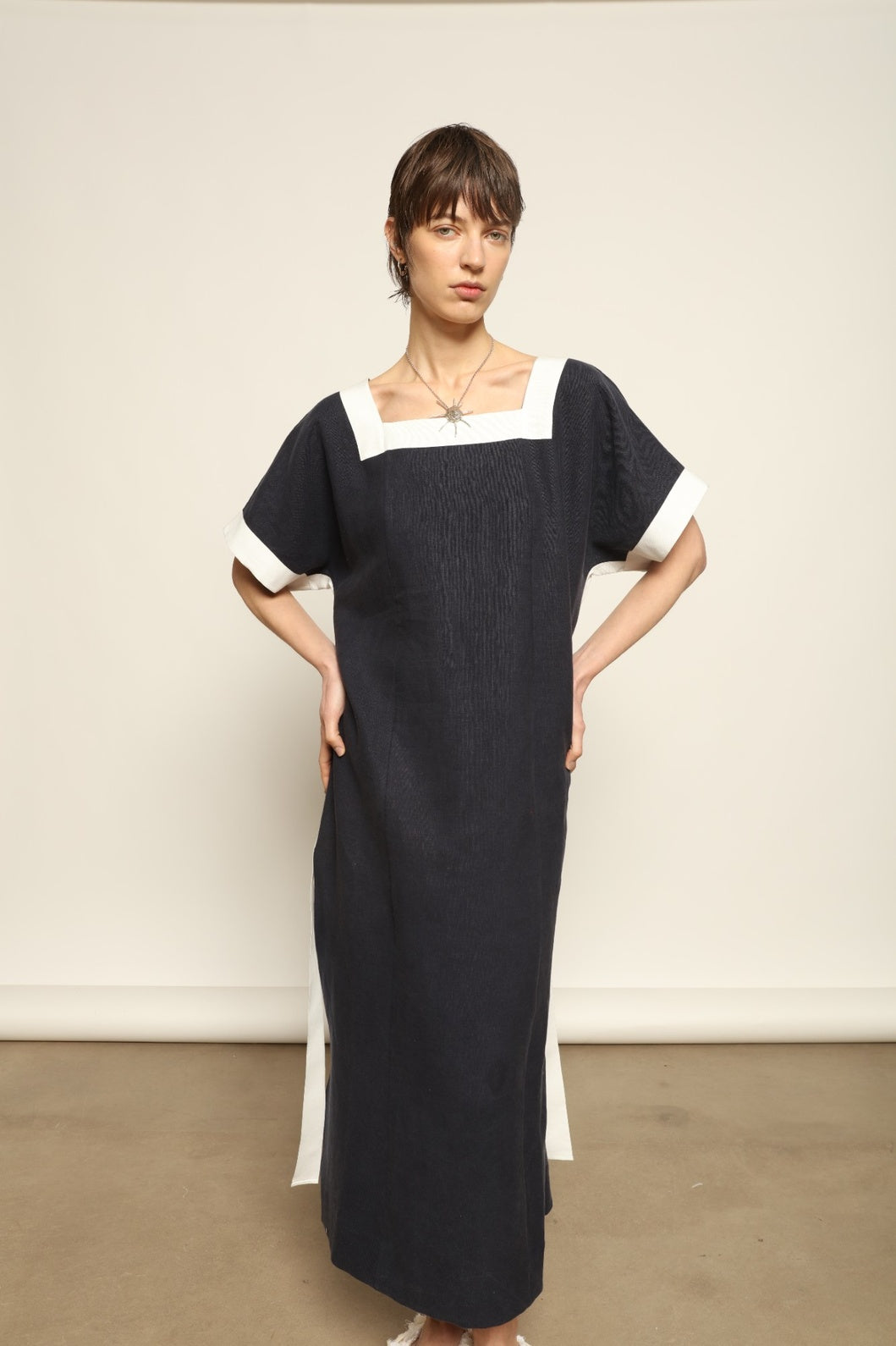 Model is wearing the Les Vacances d’Irina Astypalea kaftan linen dress in white with navy ribbon appliqués, handcrafted in Bucharest, from the House of Nomad Stories selection.