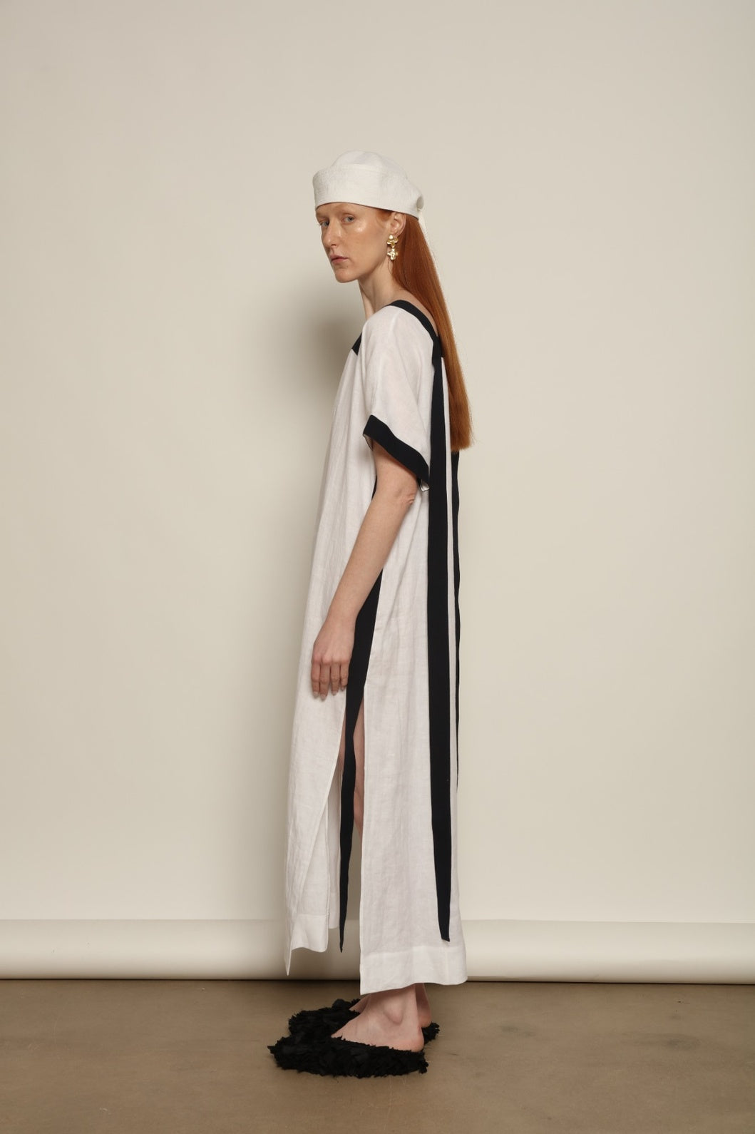 Model is wearing the Les Vacances d’Irina Astypalea kaftan linen dress in white with navy ribbon appliqués, handcrafted in Bucharest, from the House of Nomad Stories selection.