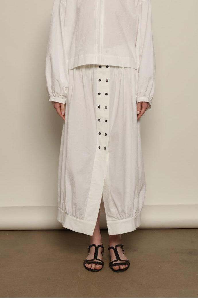 Model is wearing the Les Vacances d’Irina Jade white cotton skirt with high waist and double-breasted button front, from the House of Nomad Stories selection.