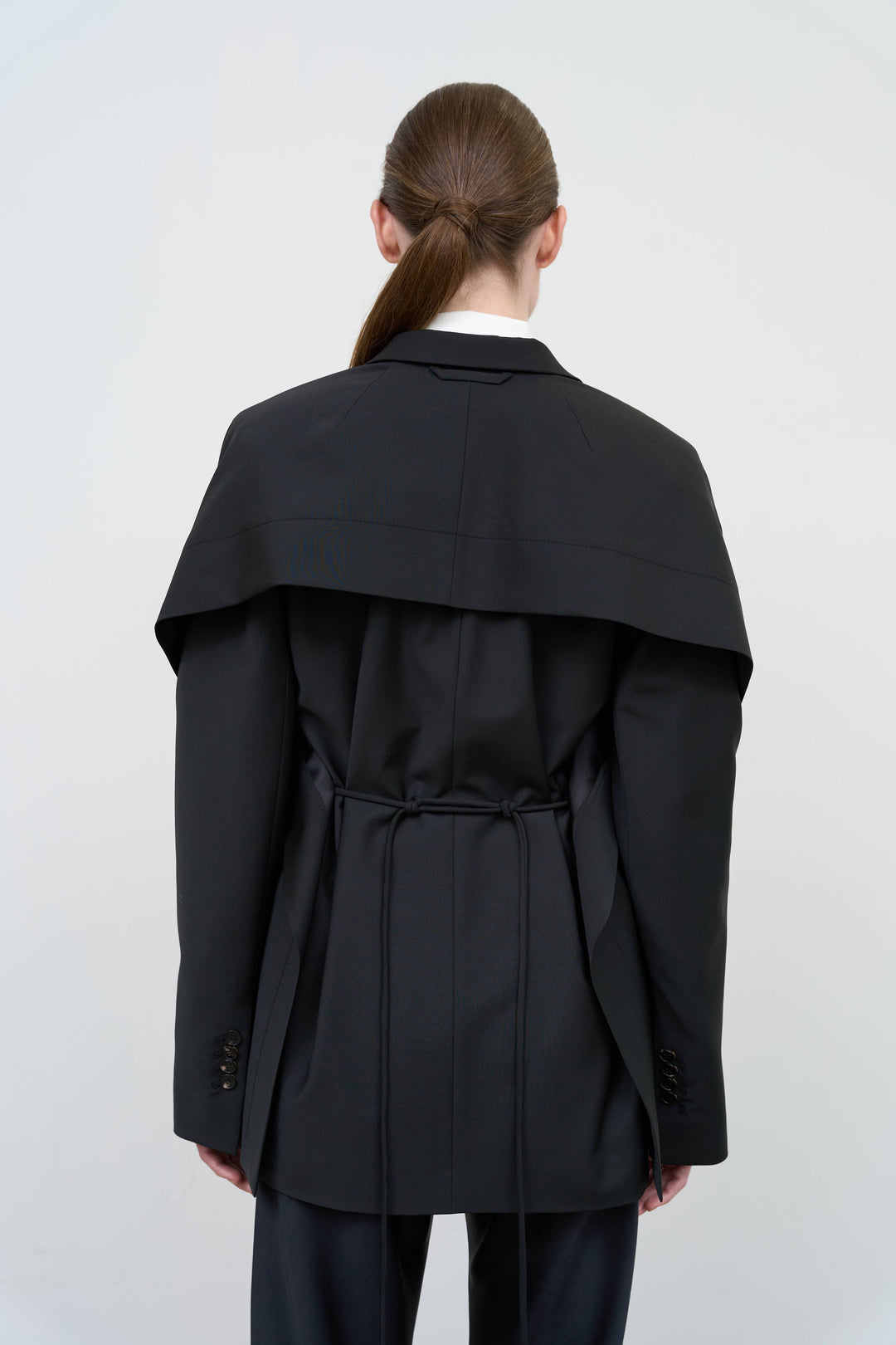 Model is wearing a black tailored wool-blend jacket by Litkovska with capelet overlay and architectural design, designer women’s jacket available at House of Woven Stories