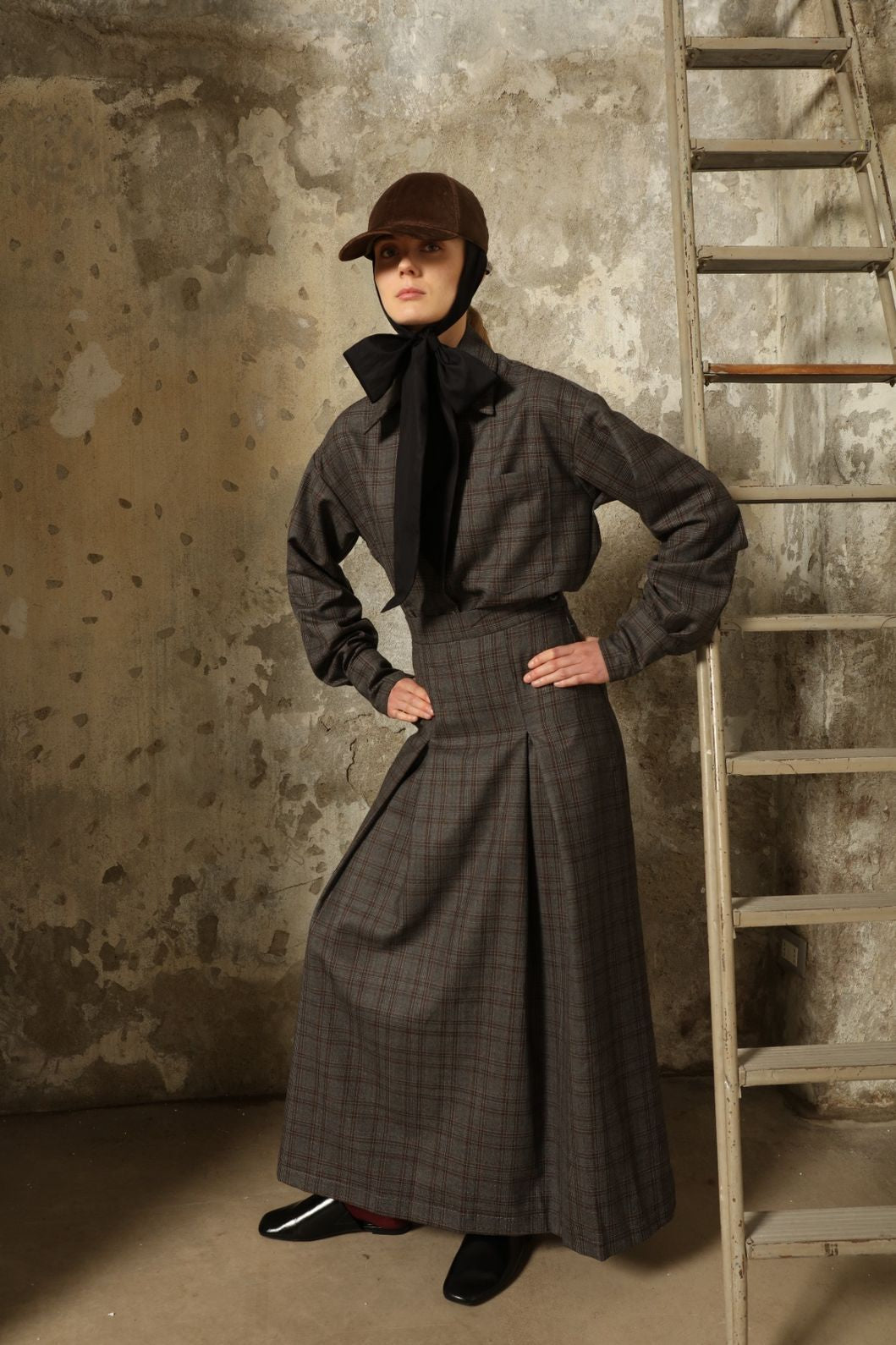 Model is wearing the Londra Brown Checked Skirt by House of Nomad Stories, ankle-length with fine pleats and brown checked pattern, combining timeless tailoring with contemporary elegance and quality craftsmanship.
