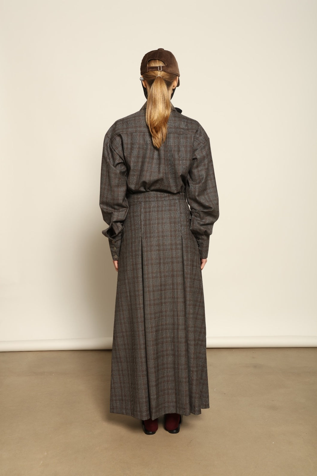 Model is wearing the Londra Brown Checked Skirt by House of Nomad Stories, ankle-length with fine pleats and brown checked pattern, combining timeless tailoring with contemporary elegance and quality craftsmanship.