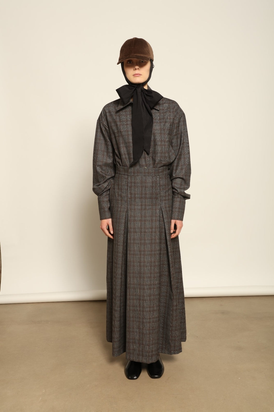 Model is wearing the Londra Brown Checked Skirt by House of Nomad Stories, ankle-length with fine pleats and brown checked pattern, combining timeless tailoring with contemporary elegance and quality craftsmanship.