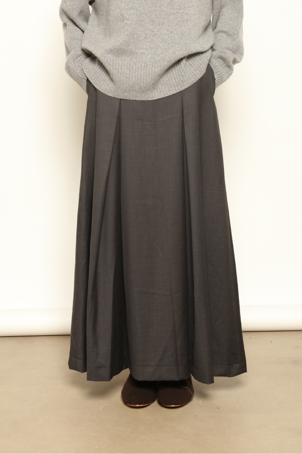 Model is wearing the Londra Grey Merino Wool Skirt by House of Nomad Stories – crafted in Italy with subtle pleats, a flattering structured silhouette, and soft grey tones for timeless elegance.