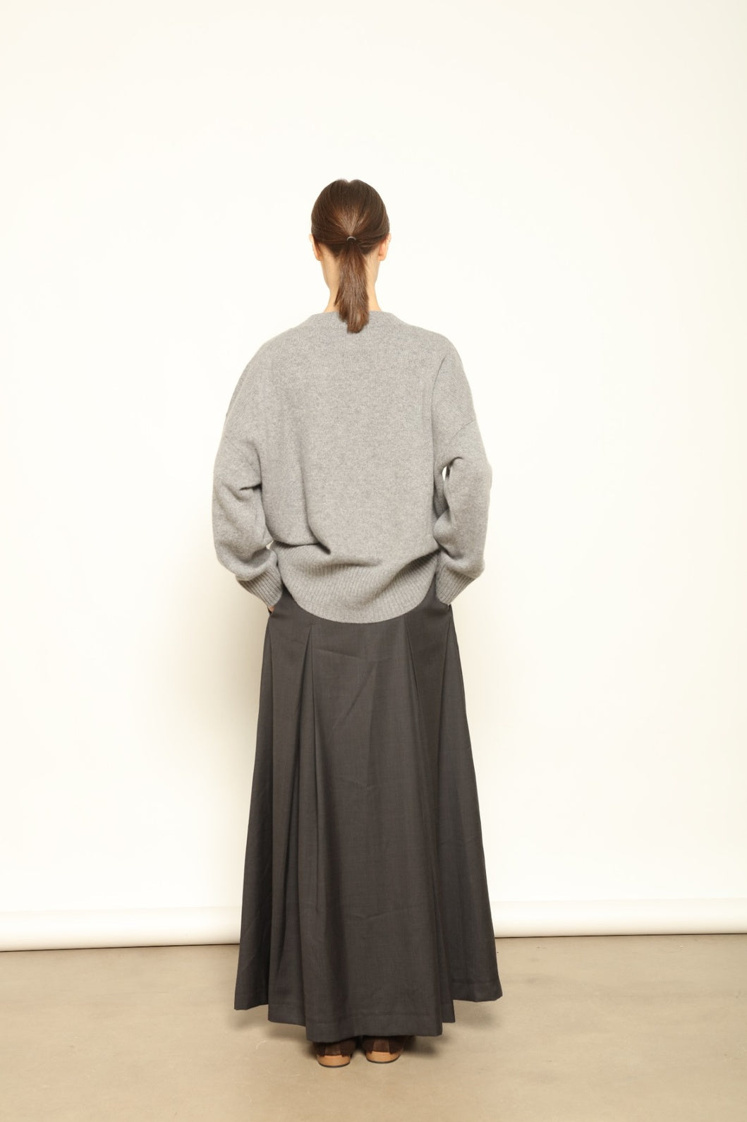 Model is wearing the Londra Grey Merino Wool Skirt by House of Nomad Stories – crafted in Italy with subtle pleats, a flattering structured silhouette, and soft grey tones for timeless elegance.