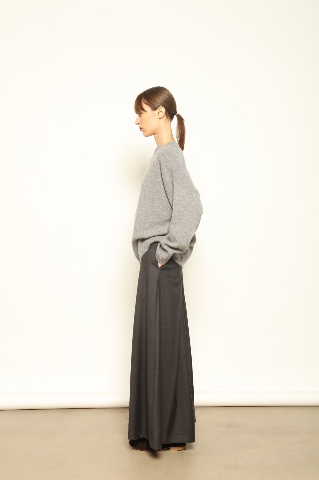 Model is wearing the Londra Grey Merino Wool Skirt by House of Nomad Stories – crafted in Italy with subtle pleats, a flattering structured silhouette, and soft grey tones for timeless elegance.