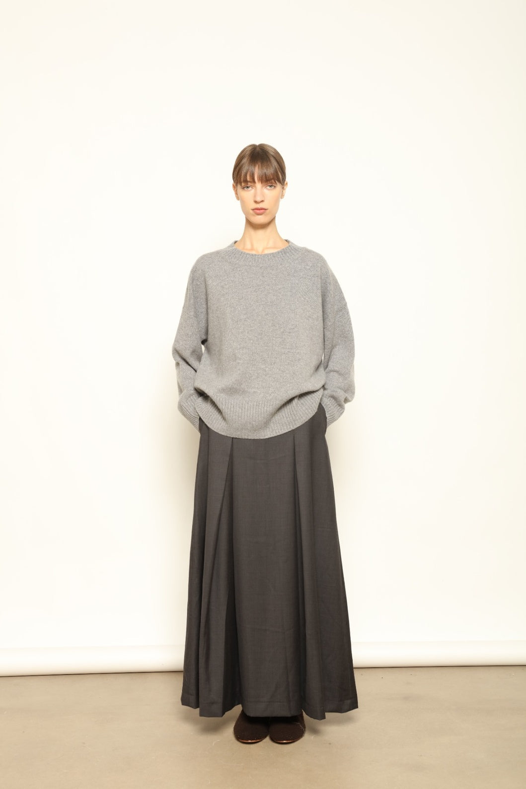 Model is wearing the Londra Grey Merino Wool Skirt by House of Nomad Stories – crafted in Italy with subtle pleats, a flattering structured silhouette, and soft grey tones for timeless elegance.