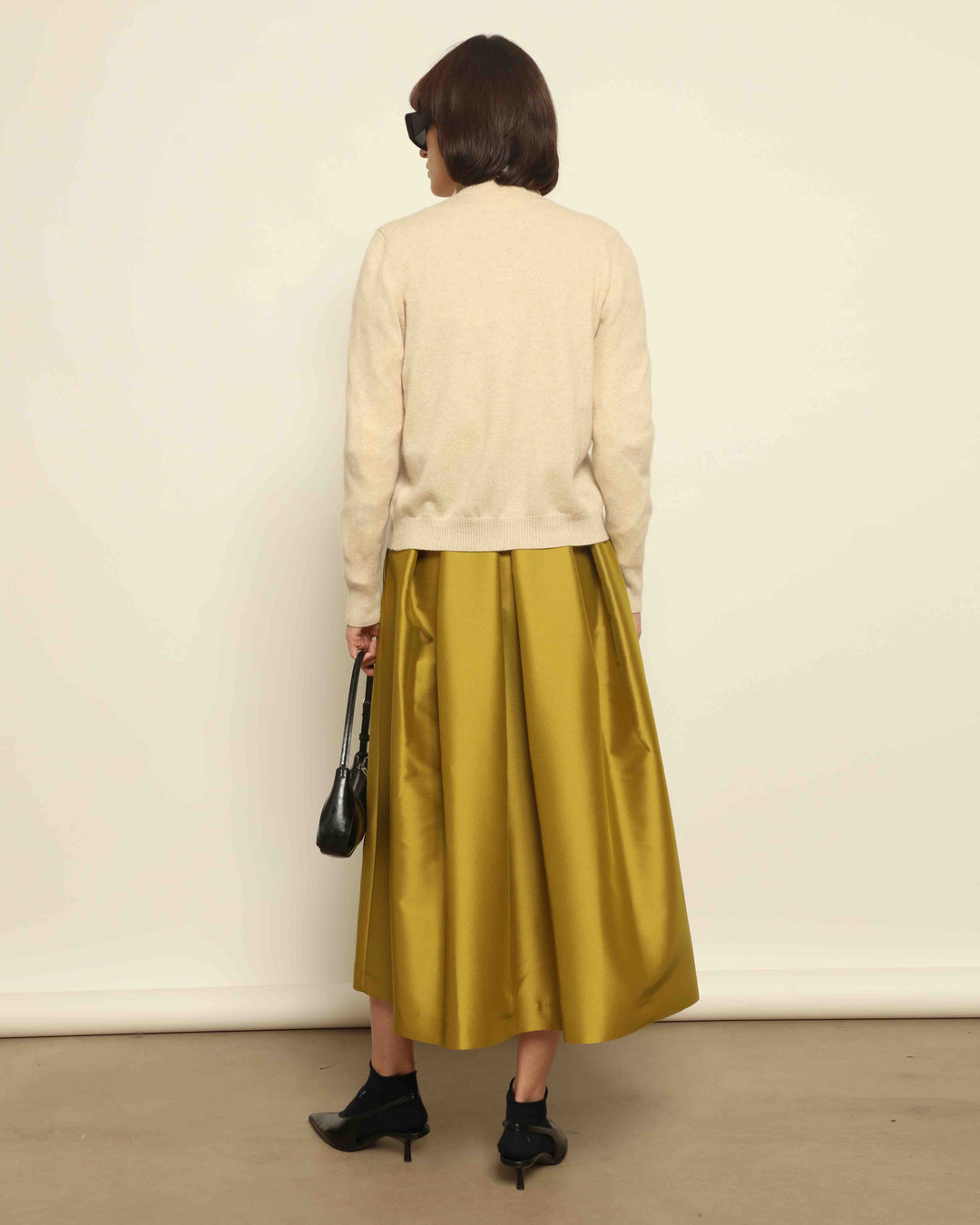 Model is wearing Duchesse Oliva Skirt by Lunatica Milano available at House of Nomad Stories. Pleated maxi skirt in a luxurious soft-blend fabric. Elegant, feminine, and handmade in Italy.