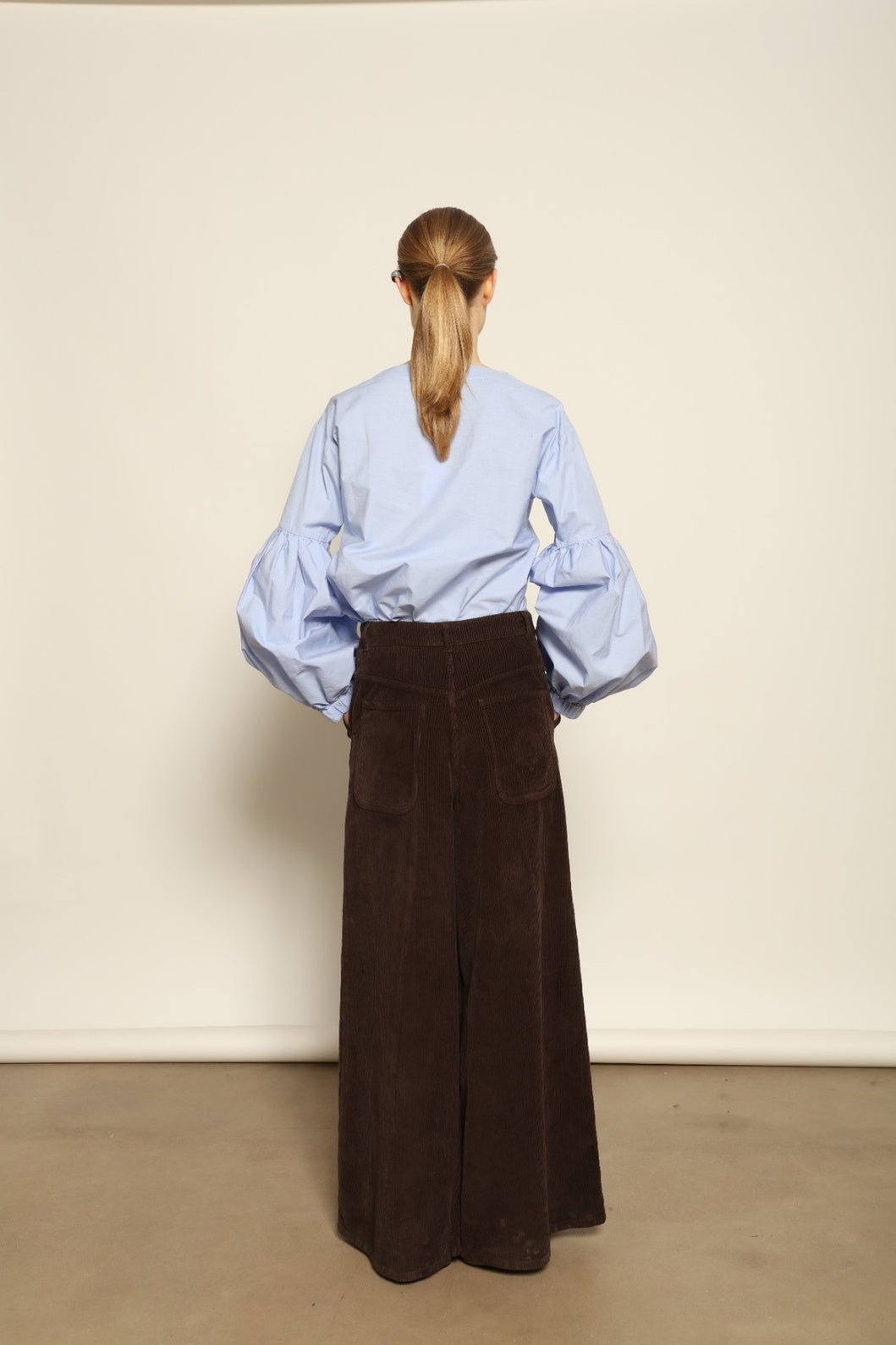 Model is wearing the Maron Foncè Le Pantalon Over Chino by Happy Haus, crafted in soft velour with a wide flowing silhouette, removable belt, back embroidered peacock, and wooden button detail for versatile, relaxed-chic style.