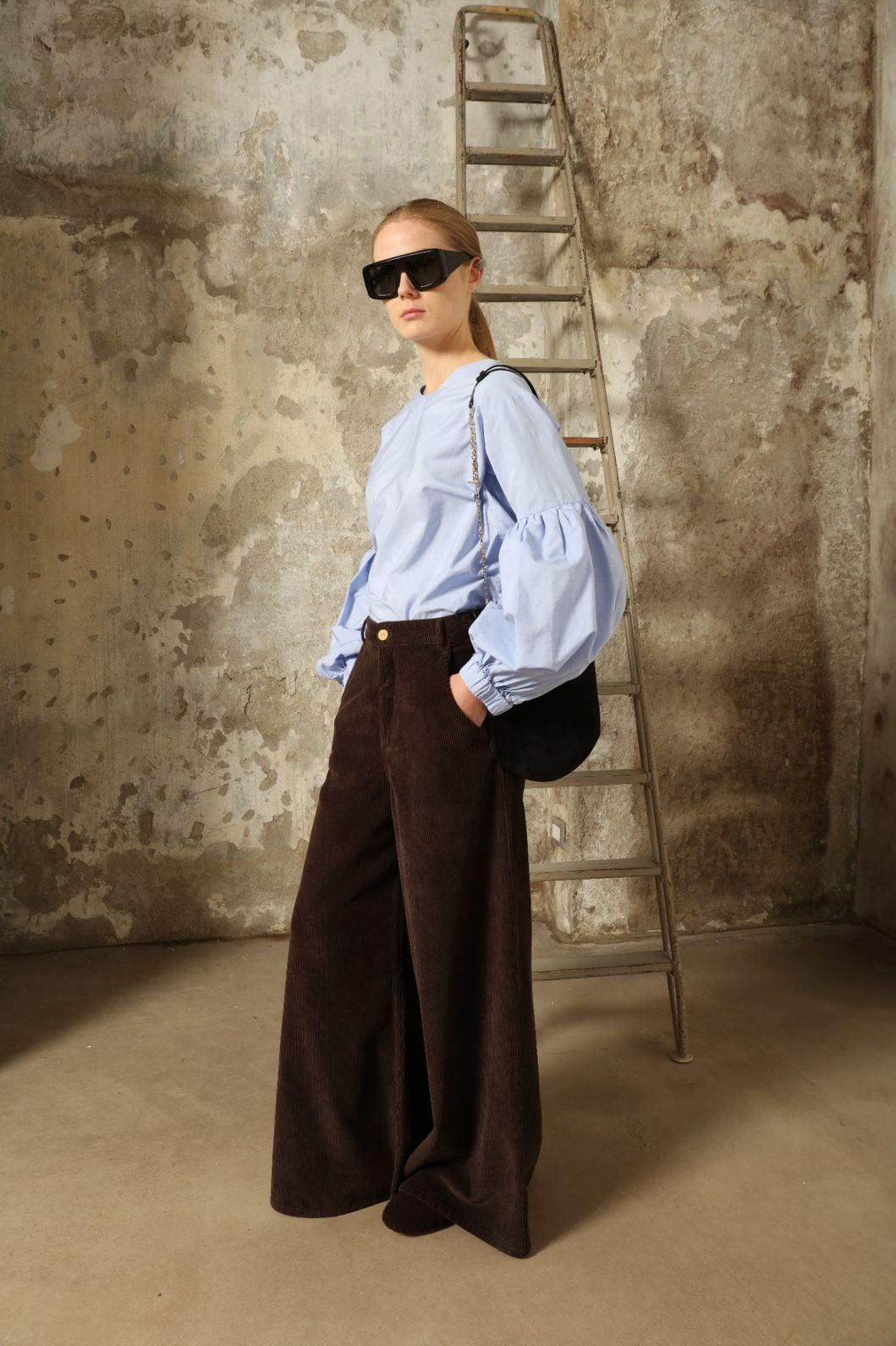 Model is wearing the Maron Foncè Le Pantalon Over Chino by Happy Haus, crafted in soft velour with a wide flowing silhouette, removable belt, back embroidered peacock, and wooden button detail for versatile, relaxed-chic style.