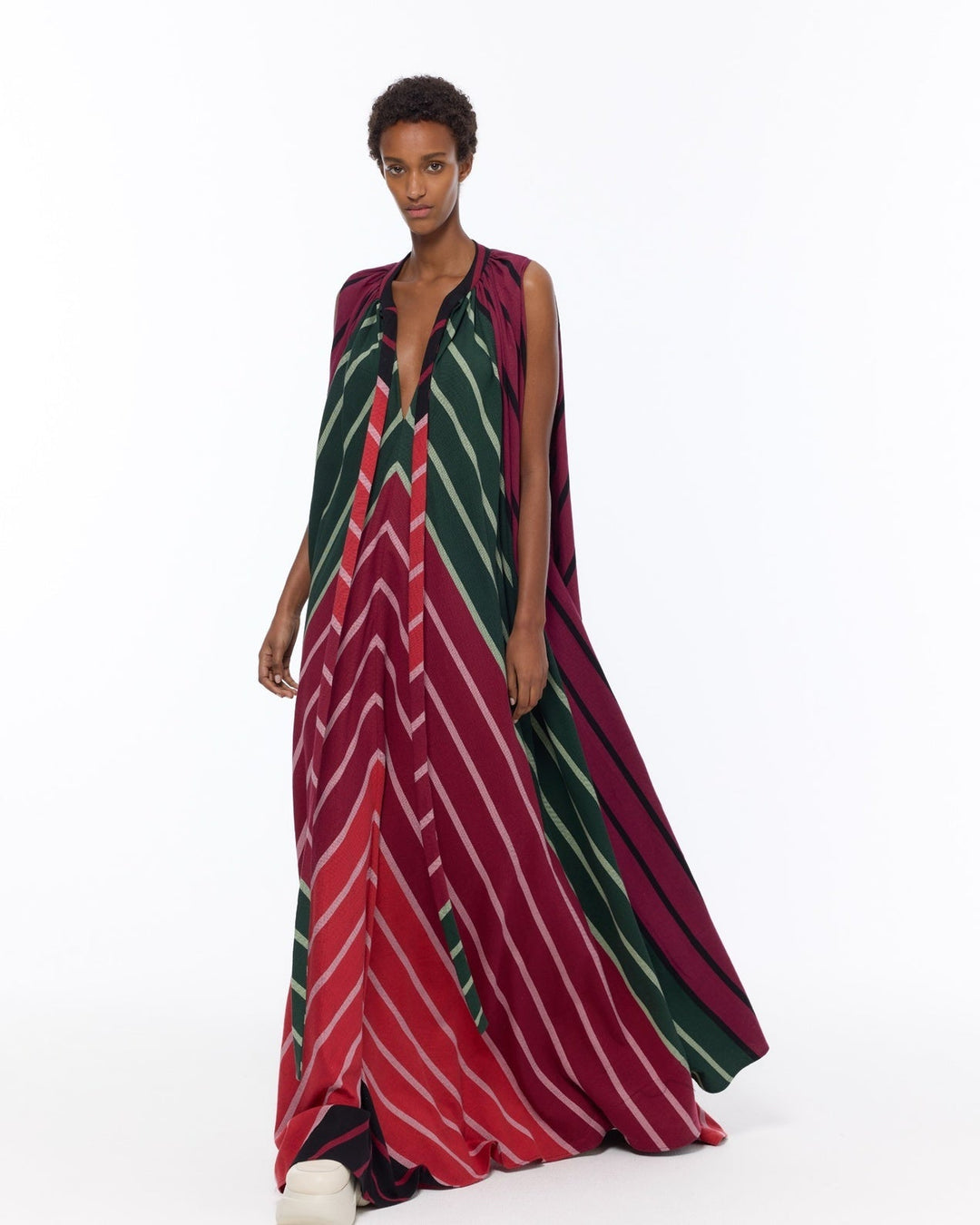 Model is wearing the Cape Dress by Marrakshi Life, a hand-woven striped dress in green and red with adjustable neckline ties and a flowing cape-like silhouette, curated in the House of Nomad Stories selection.