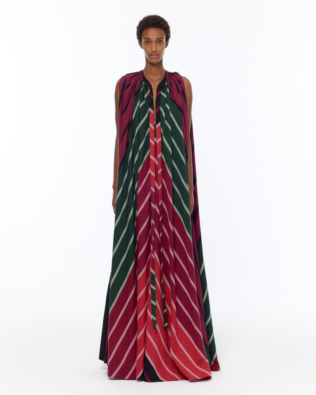 Model is wearing the Cape Dress by Marrakshi Life, a hand-woven striped dress in green and red with adjustable neckline ties and a flowing cape-like silhouette, curated in the House of Nomad Stories selection.