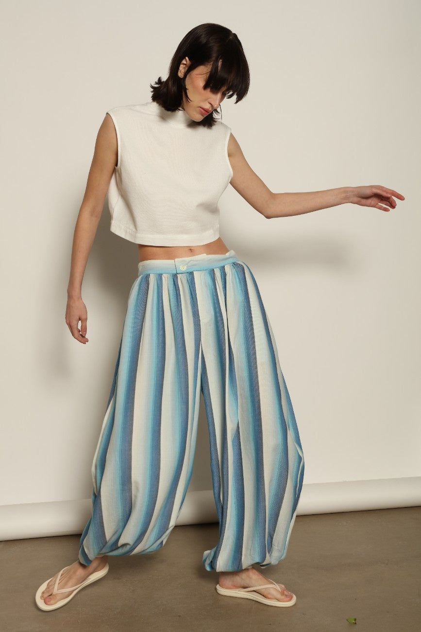Model is wearing Marrakshi Life cropped turtleneck in white hand-loomed cotton, boxy fit high neck cropped top with minimalist design styled with high-waisted trousers