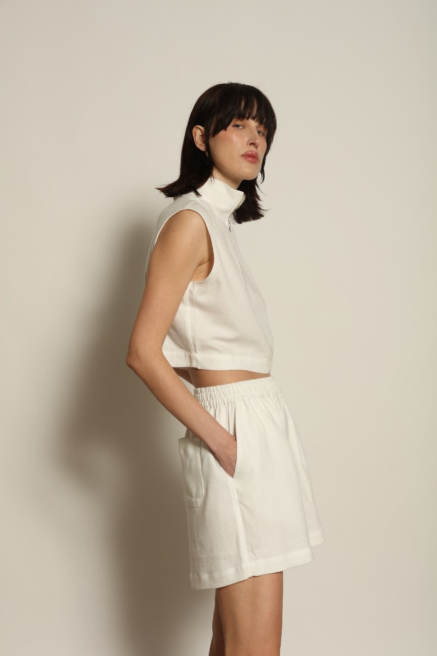 Model is wearing Marrakshi Life cropped turtleneck in white hand-loomed cotton, boxy fit high neck cropped top with minimalist design styled with high-waisted trousers
