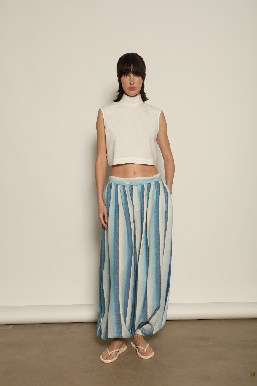 Model is wearing Marrakshi Life cropped turtleneck in white hand-loomed cotton, boxy fit high neck cropped top with minimalist design styled with high-waisted trousers