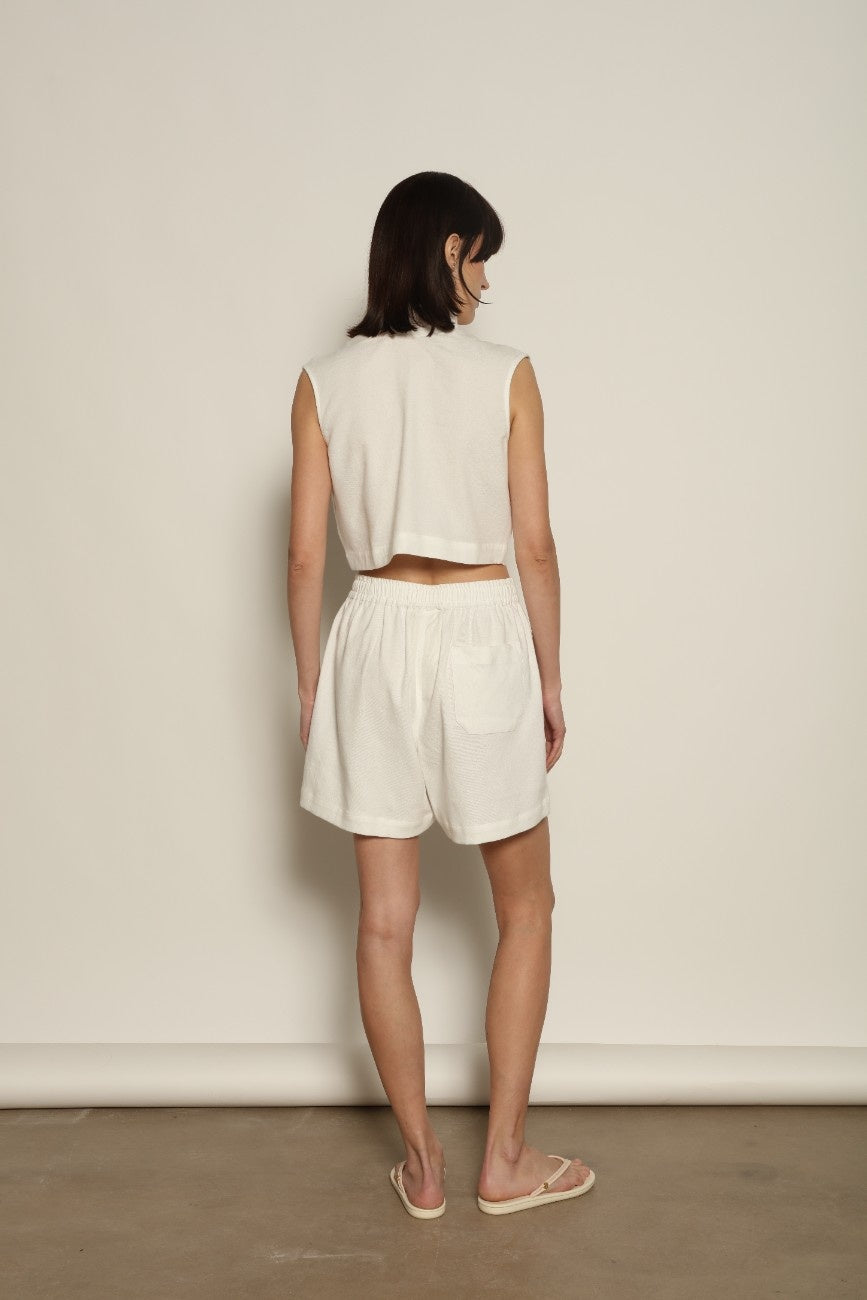 Model is wearing Marrakshi Life cropped turtleneck in white hand-loomed cotton, boxy fit high neck cropped top with minimalist design styled with high-waisted trousers