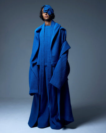 Model is wearing the French Blue Bouclé Blanket Coat by Marrakshi Life, a hand-woven oversized cotton bouclé coat with a deep shawl collar and textured finish, curated in the House of Nomad Stories selection.