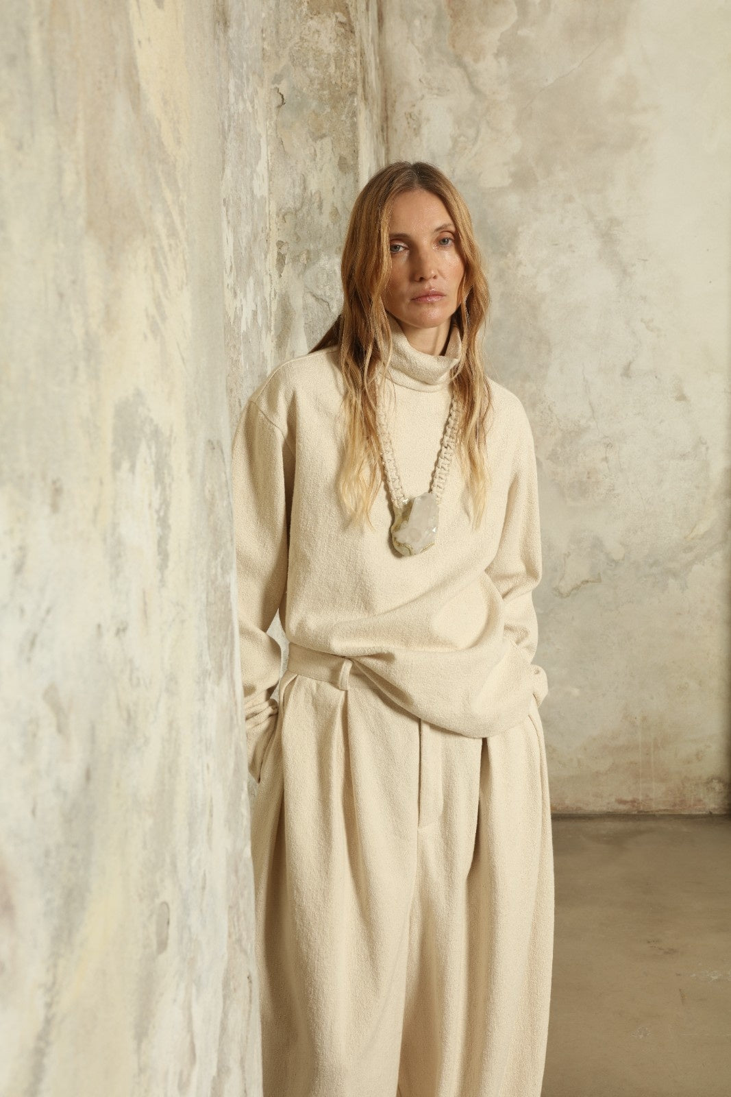 Model is wearing the Mid Rise Ecru Boucle Solid Pant by Marrakshi Life, part of House of Nomad Stories collection, handwoven cotton boucle pants with mid-rise fit, front pleats, and wide flowing leg
