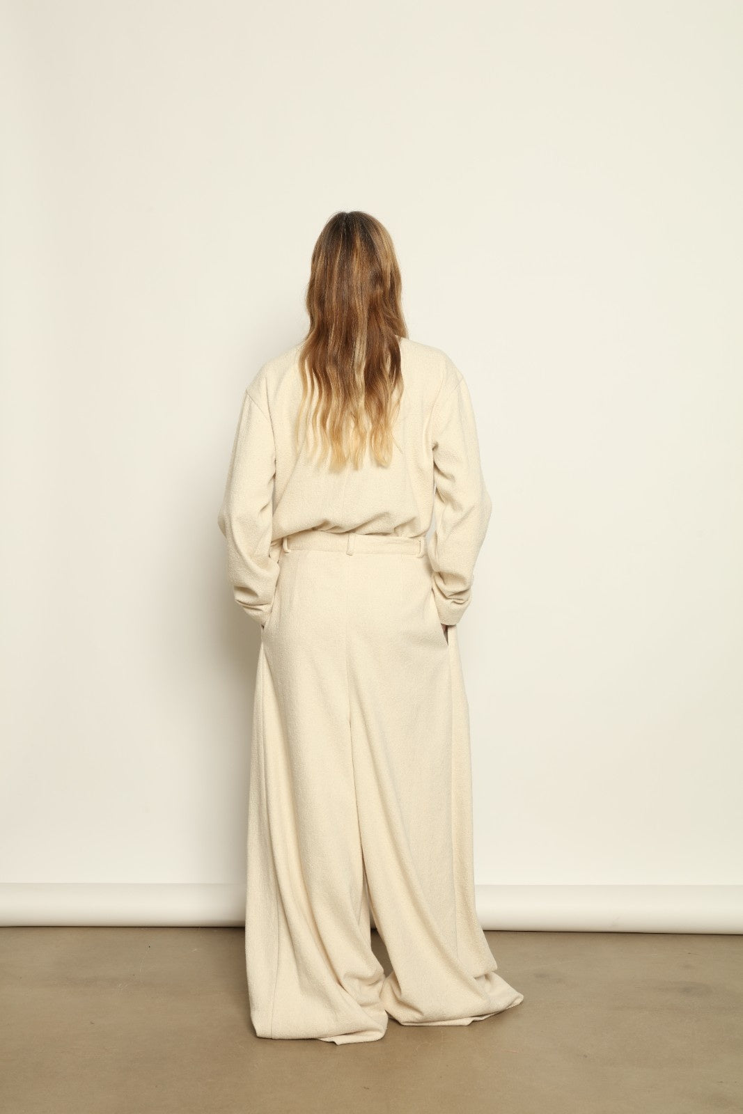 Model is wearing the Mid Rise Ecru Boucle Solid Pant by Marrakshi Life, part of House of Nomad Stories collection, handwoven cotton boucle pants with mid-rise fit, front pleats, and wide flowing leg