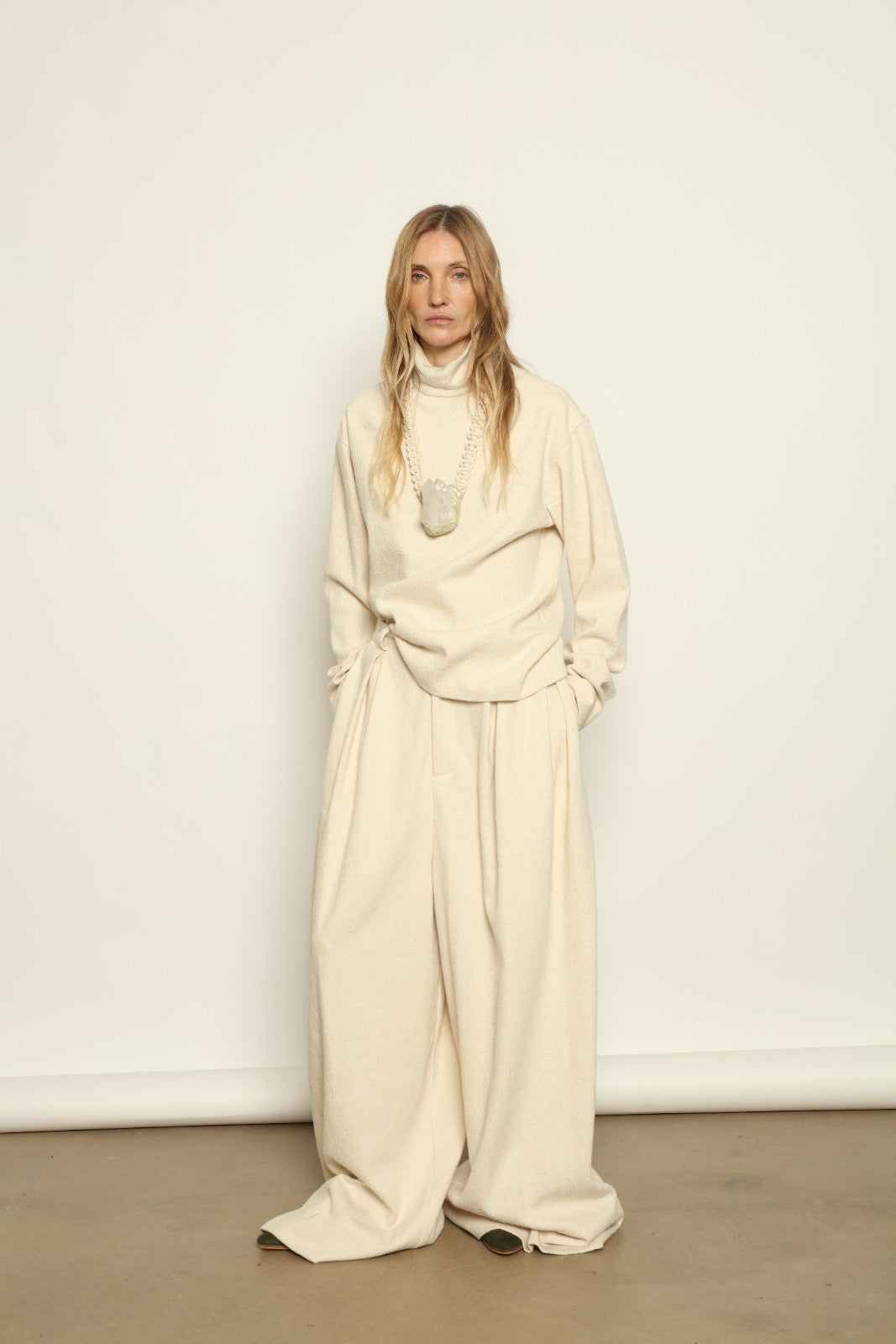 Model is wearing the Mid Rise Ecru Boucle Solid Pant by Marrakshi Life, part of House of Nomad Stories collection, handwoven cotton boucle pants with mid-rise fit, front pleats, and wide flowing leg