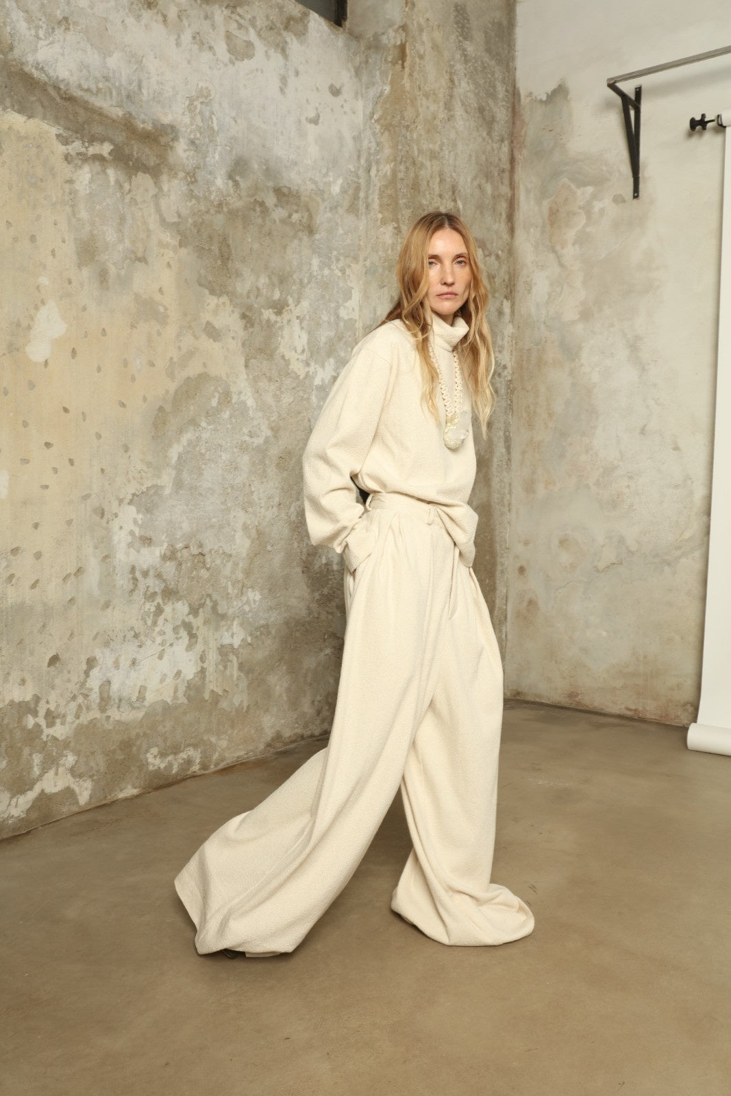 Model is wearing the Mid Rise Ecru Boucle Solid Pant by Marrakshi Life, part of House of Nomad Stories collection, handwoven cotton boucle pants with mid-rise fit, front pleats, and wide flowing leg
