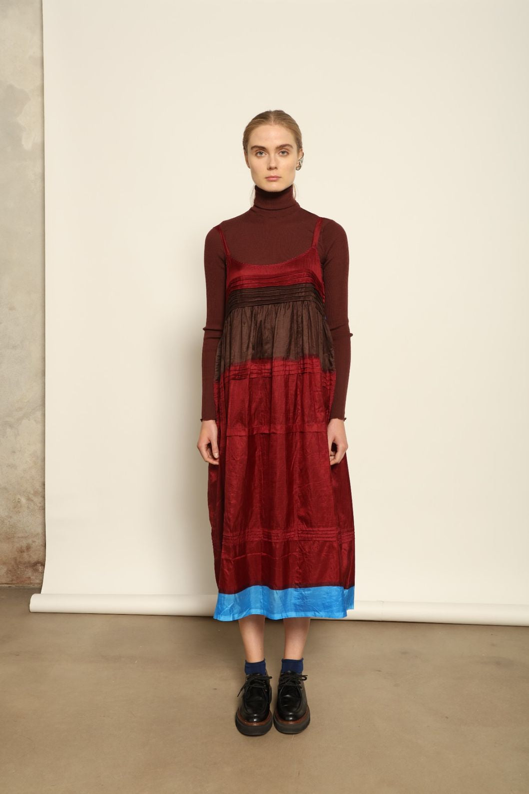 Model is wearing the Miraj 95 Silk and Cotton Slip Dress by Injiri, crafted in red and brown cotton with silk accents and a bold blue border, combining lightness, color, and refined craftsmanship.