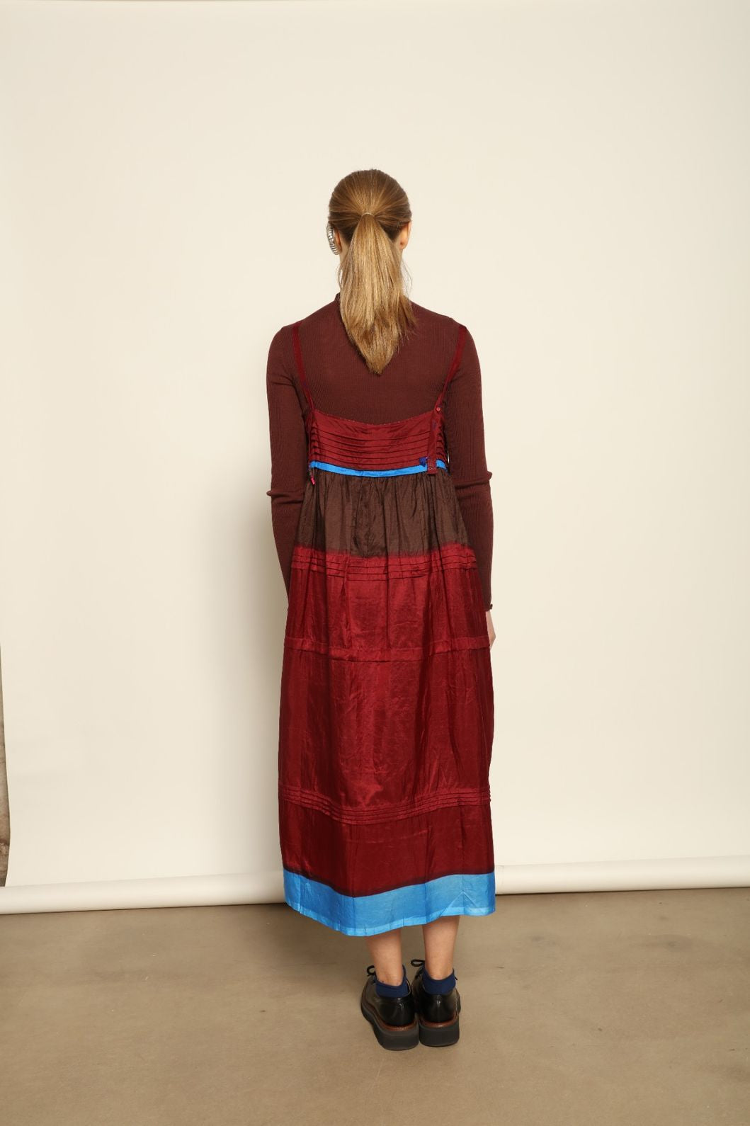 Model is wearing the Miraj 95 Silk and Cotton Slip Dress by Injiri, crafted in red and brown cotton with silk accents and a bold blue border, combining lightness, color, and refined craftsmanship.