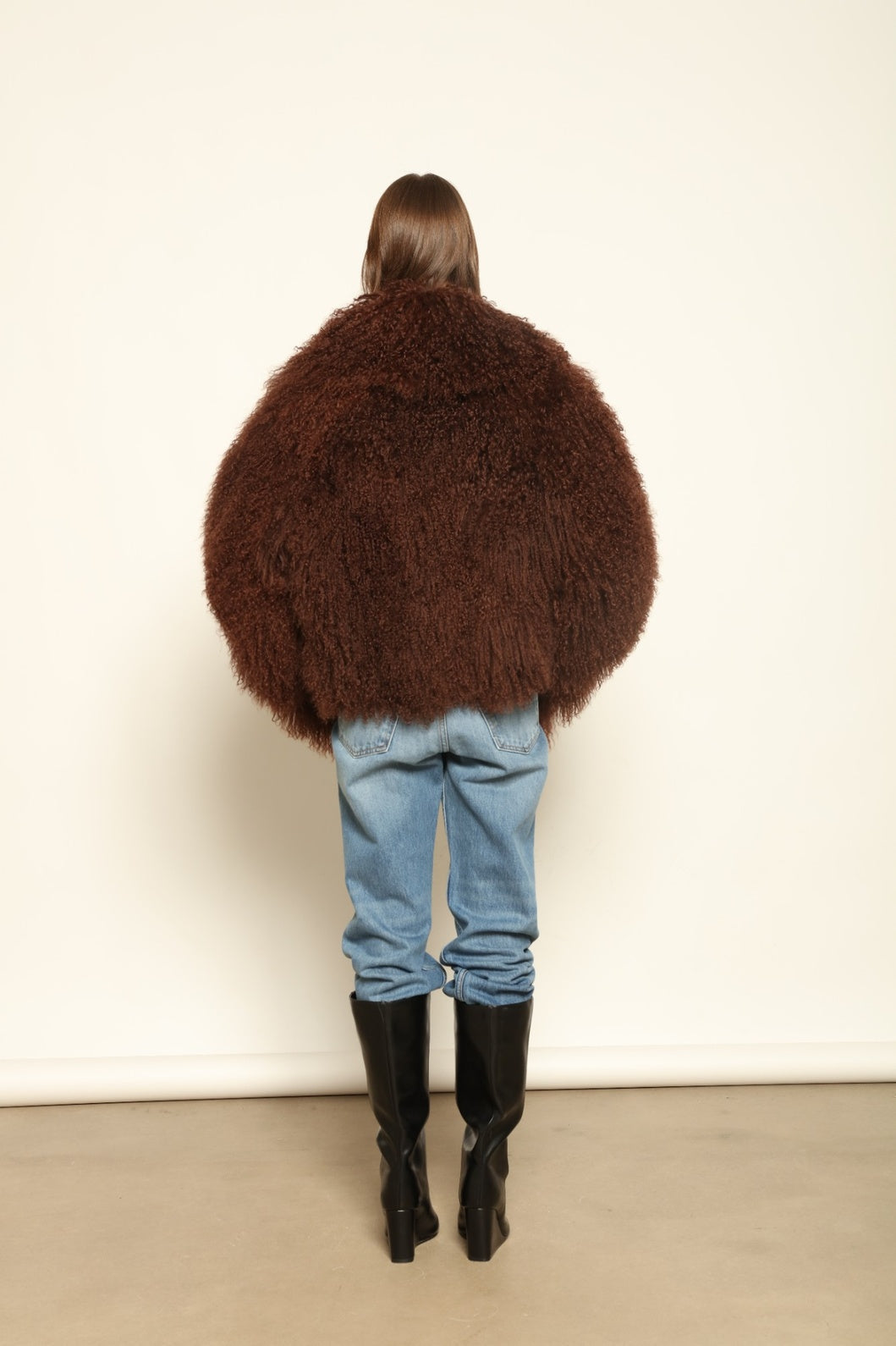 Model is wearing the Mongolia Chocolate Shearling Jacket by Blancha – crafted from 100% Tibetan lamb with pure silk lining, featuring a soft voluminous texture, deep chocolate hue, and luxurious Italian craftsmanship for feather-light warmth and timeless elegance.