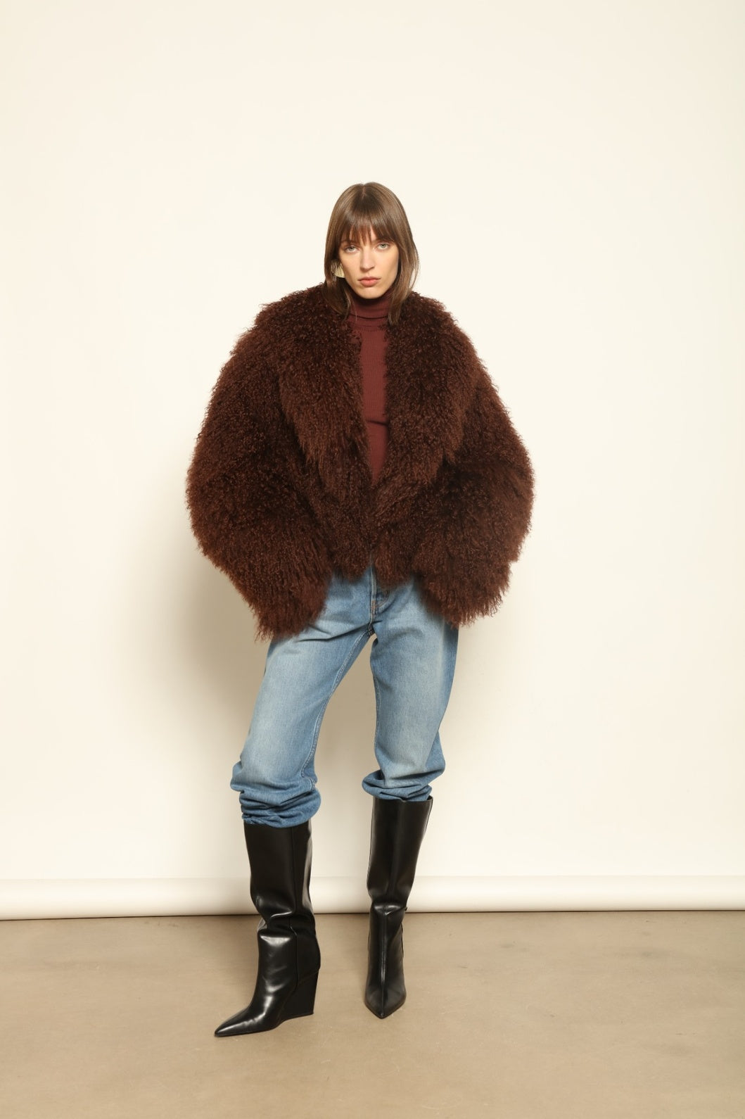 Model is wearing the Mongolia Chocolate Shearling Jacket by Blancha – crafted from 100% Tibetan lamb with pure silk lining, featuring a soft voluminous texture, deep chocolate hue, and luxurious Italian craftsmanship for feather-light warmth and timeless elegance.