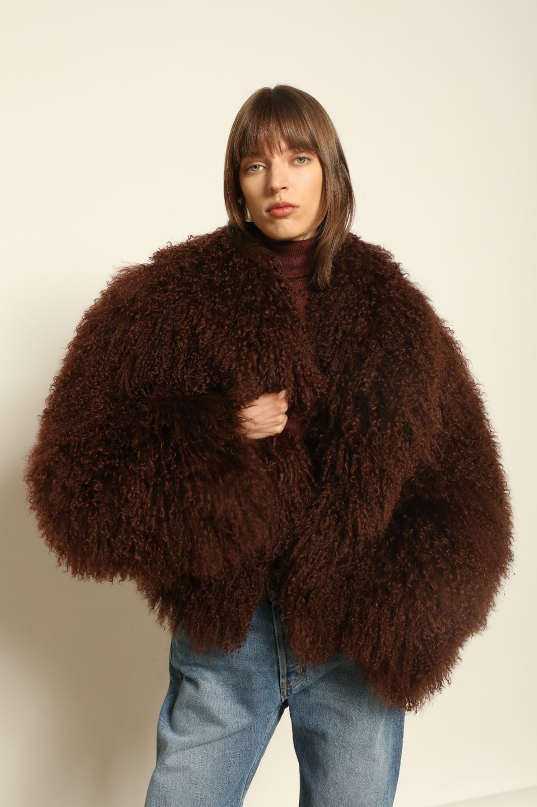 Model is wearing the Mongolia Chocolate Shearling Jacket by Blancha – crafted from 100% Tibetan lamb with pure silk lining, featuring a soft voluminous texture, deep chocolate hue, and luxurious Italian craftsmanship for feather-light warmth and timeless elegance.