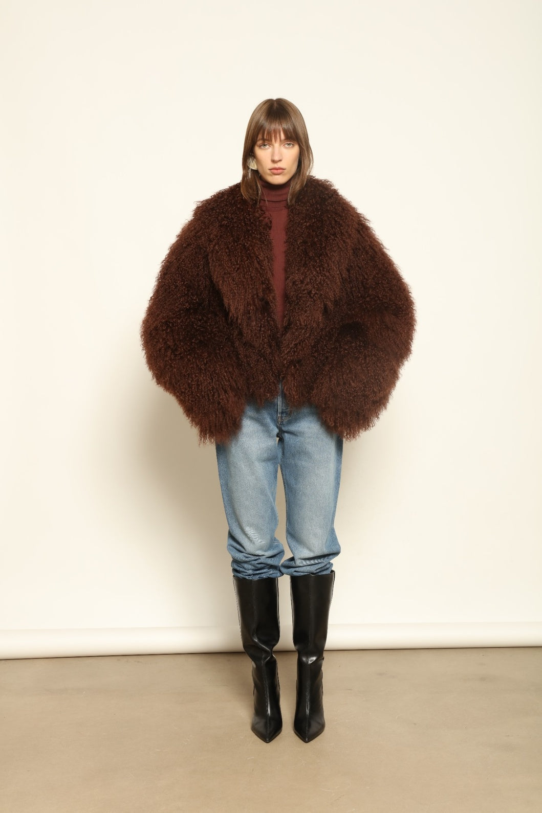 Model is wearing the Mongolia Chocolate Shearling Jacket by Blancha – crafted from 100% Tibetan lamb with pure silk lining, featuring a soft voluminous texture, deep chocolate hue, and luxurious Italian craftsmanship for feather-light warmth and timeless elegance.