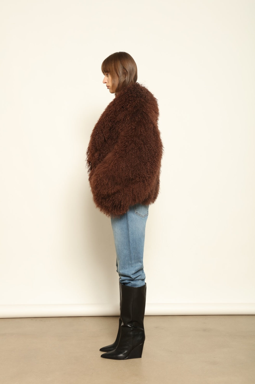 Model is wearing the Mongolia Chocolate Shearling Jacket by Blancha – crafted from 100% Tibetan lamb with pure silk lining, featuring a soft voluminous texture, deep chocolate hue, and luxurious Italian craftsmanship for feather-light warmth and timeless elegance.