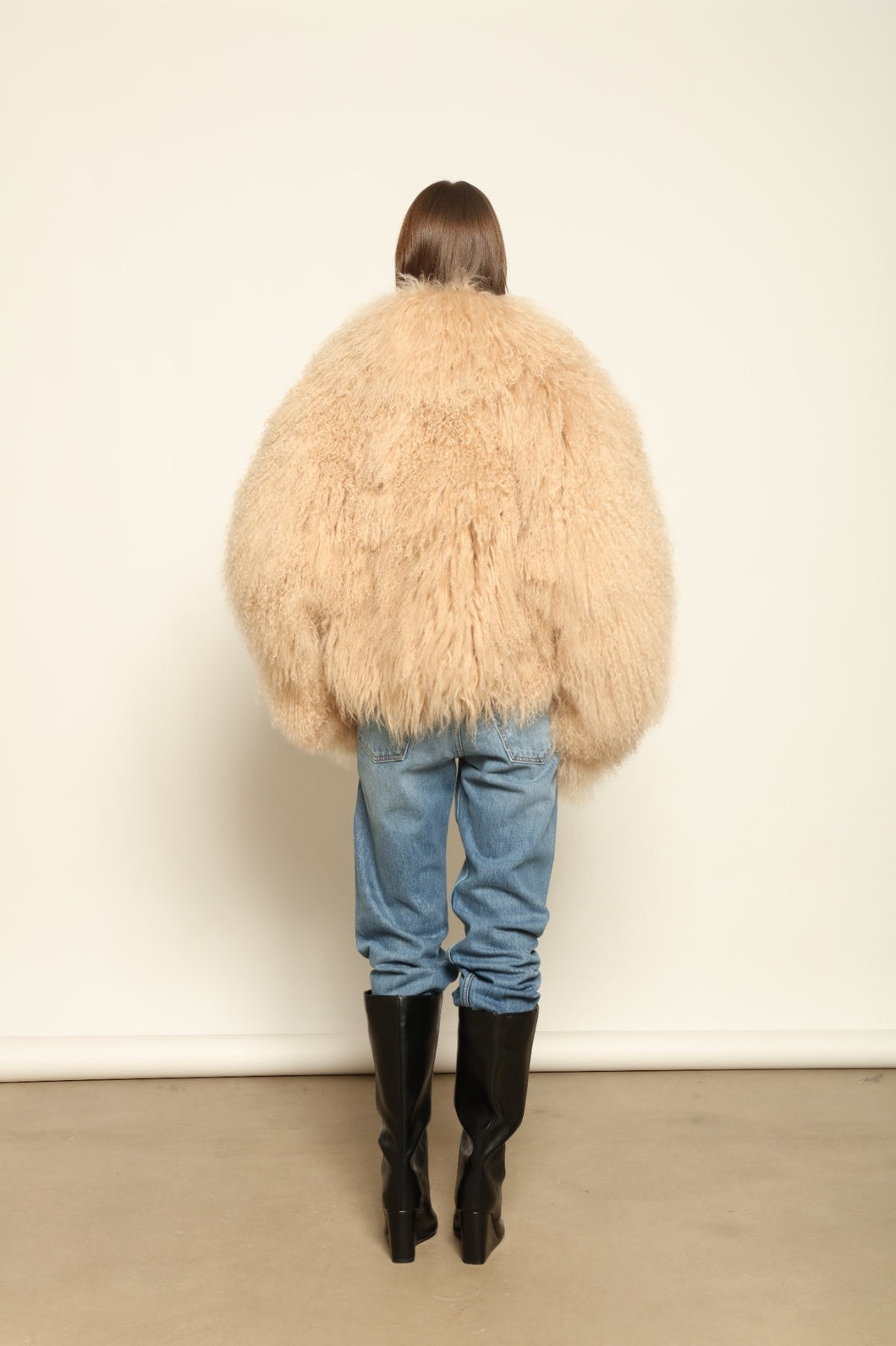 Model is wearing the Mongolia Camel Shearling Jacket by Blancha – crafted from 100% Tibetan lamb with a pure silk lining, featuring cloud-like softness, a camel hue, and expert Italian craftsmanship for a lightweight, elegant, and timeless outerwear piece.