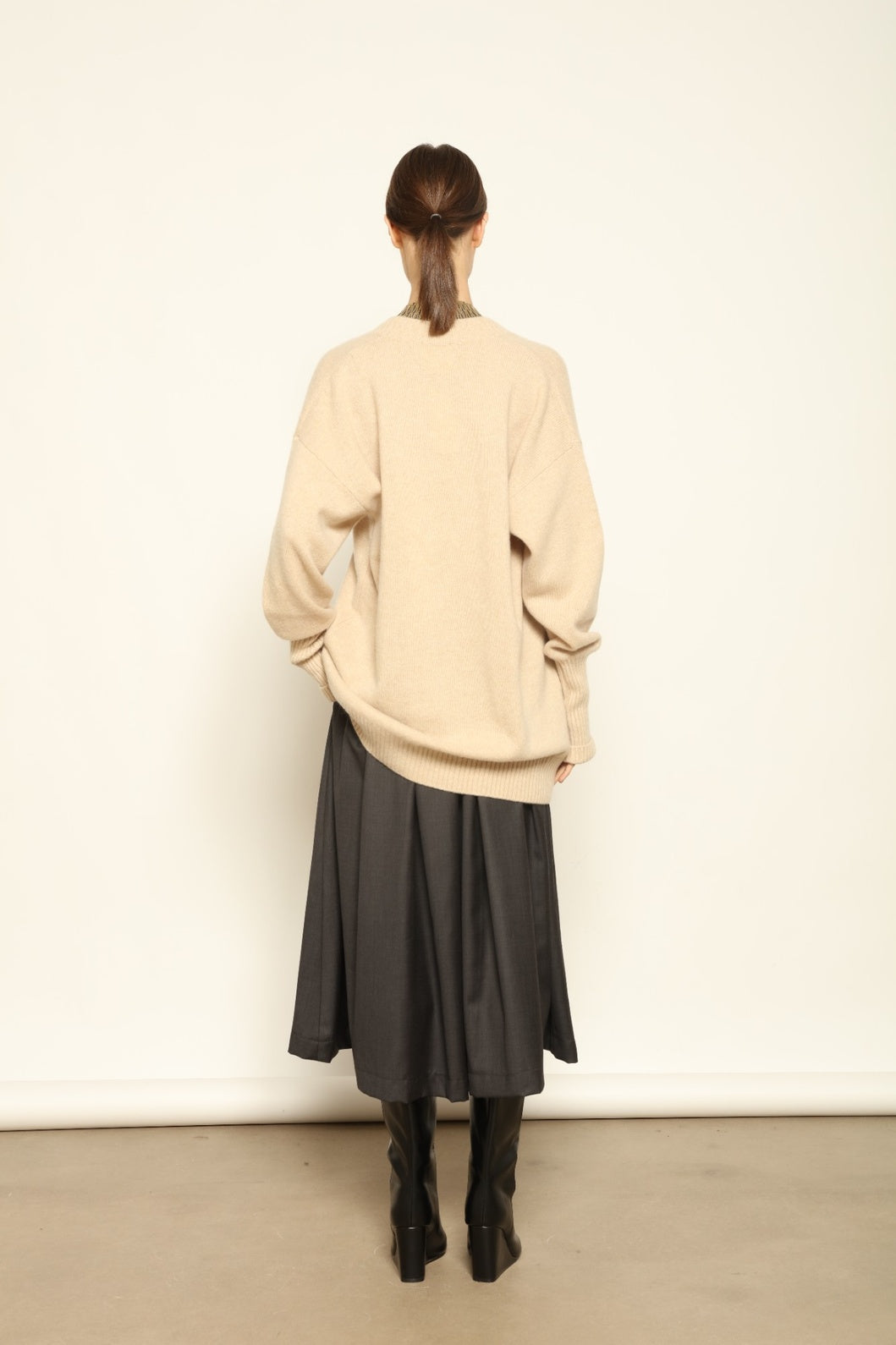 Model is wearing the Natural Nina V-Neck Long Sweater by House of Woven Stories, made from 100% pure undyed Inner Mongolia cashmere, featuring an elongated silhouette, deep V-neckline, soft breathable knit texture, and sustainable Italian craftsmanship