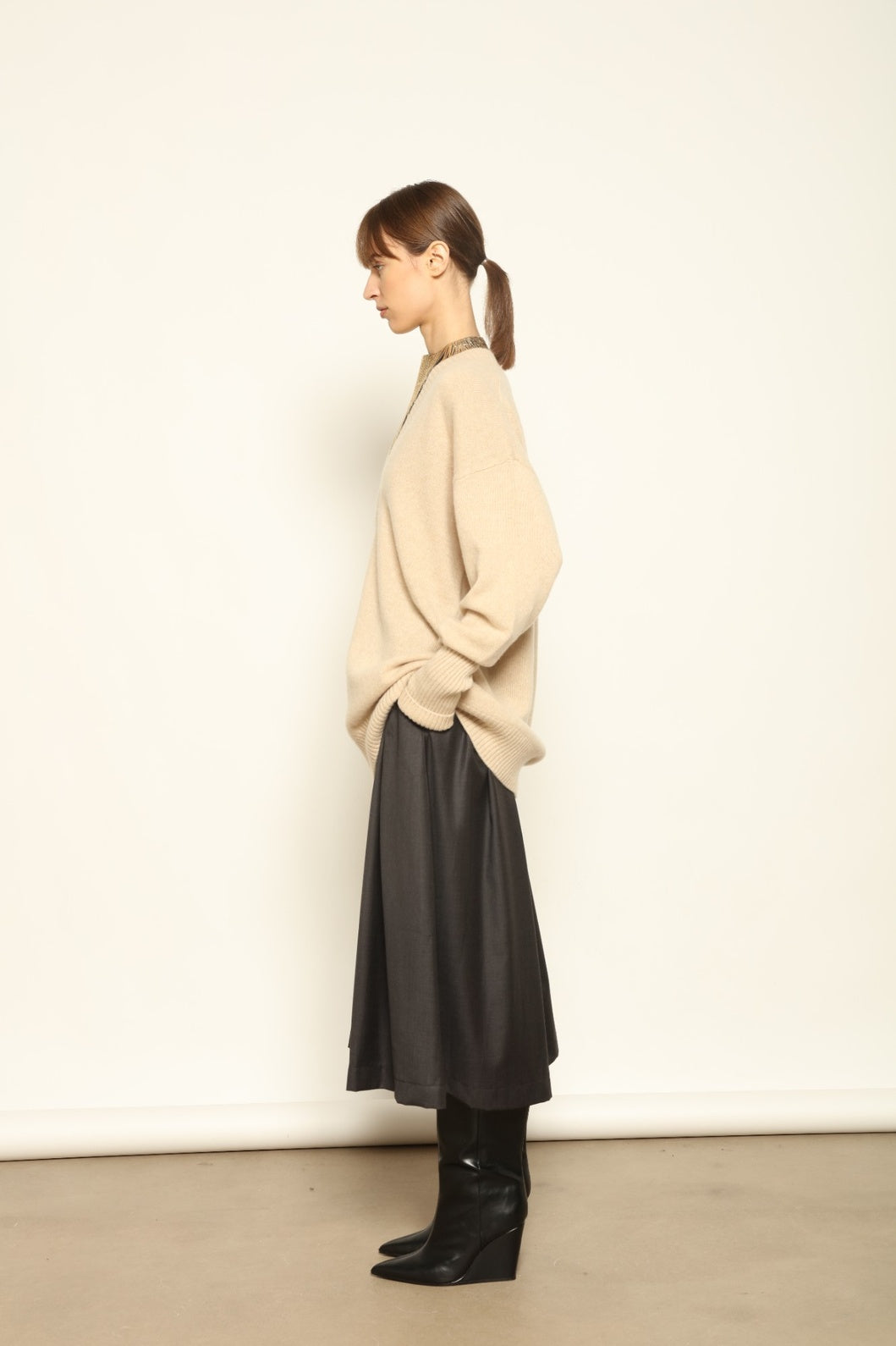 Model is wearing the Natural Nina V-Neck Long Sweater by House of Woven Stories, made from 100% pure undyed Inner Mongolia cashmere, featuring an elongated silhouette, deep V-neckline, soft breathable knit texture, and sustainable Italian craftsmanship
